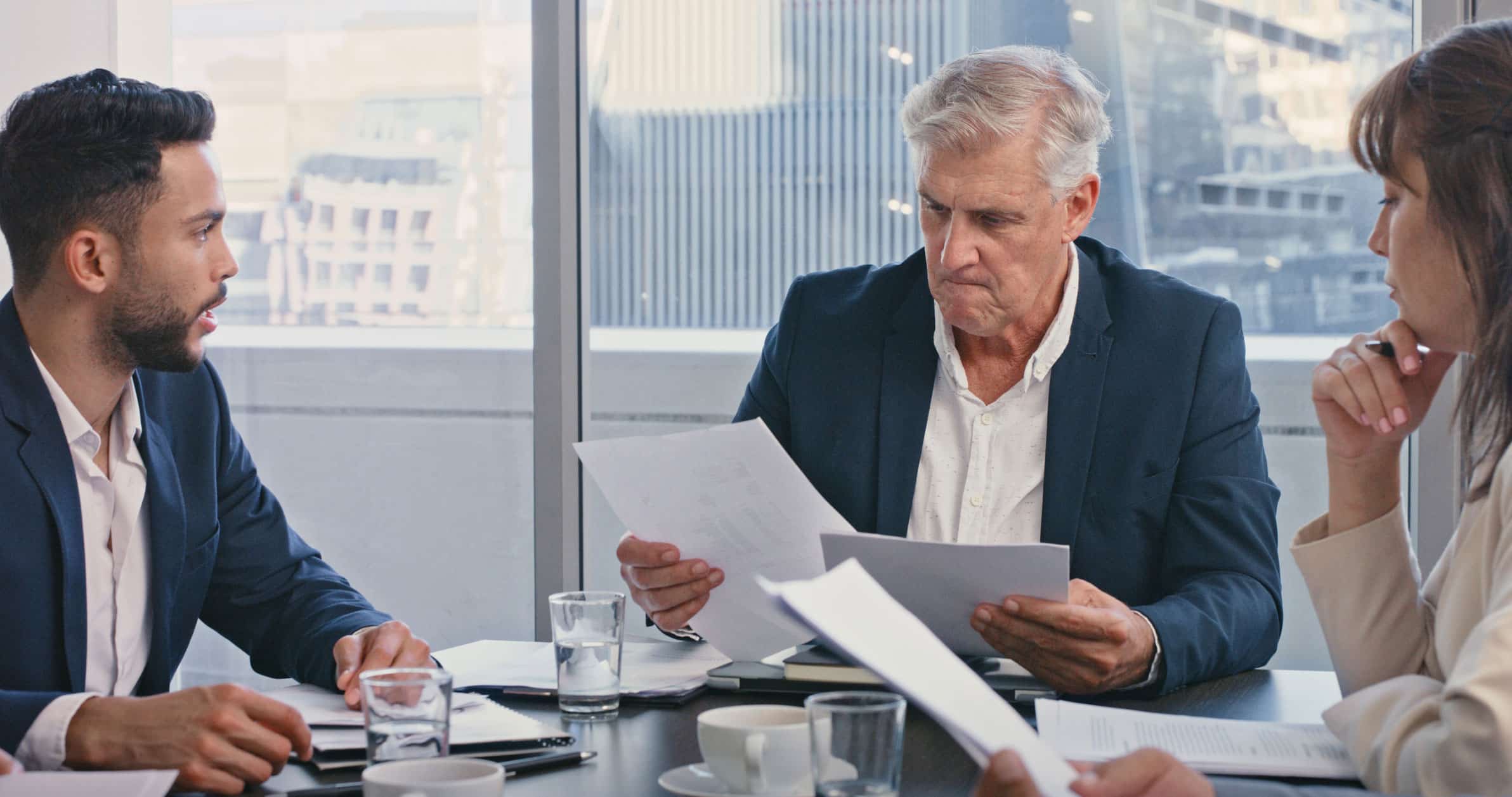 Three mergers & acquisition integration consultants review documents at an office conference table.