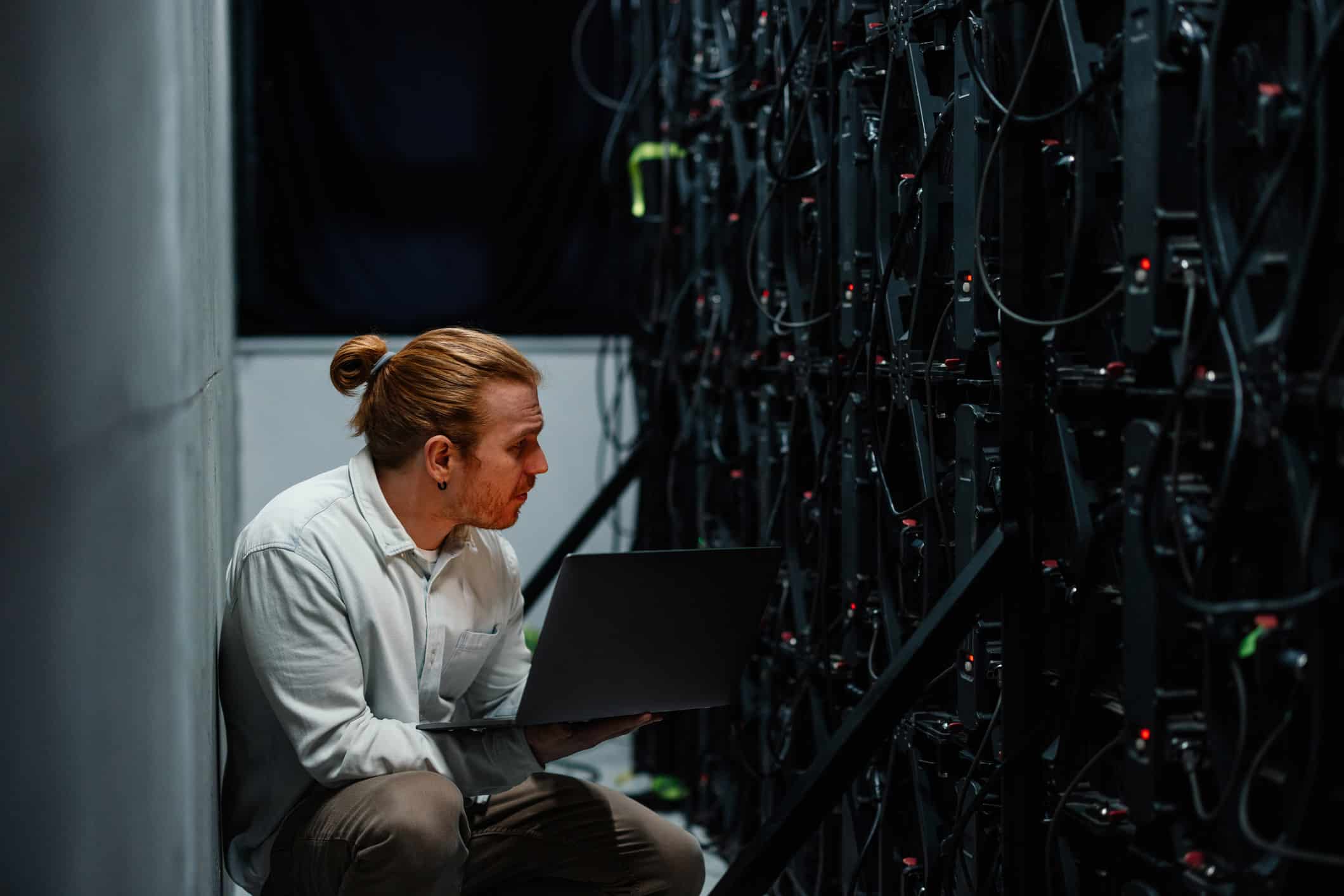 Person with laptop inspects servers in a dark data center for risk management consulting.