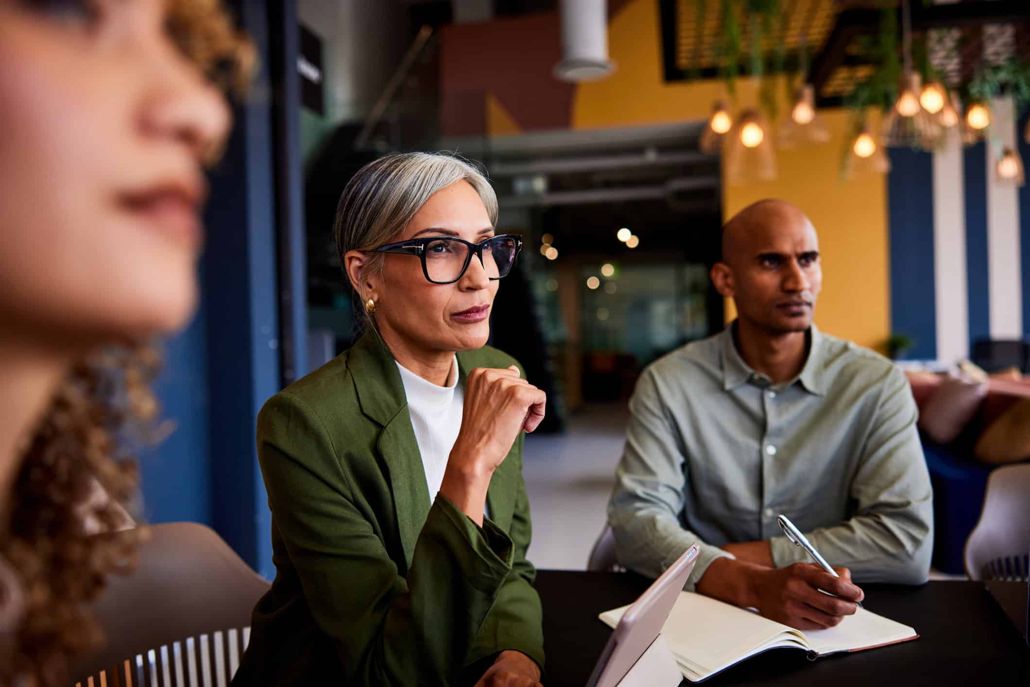 Three people in a meeting, attentively discussing Data Governance Consulting with notebooks open.