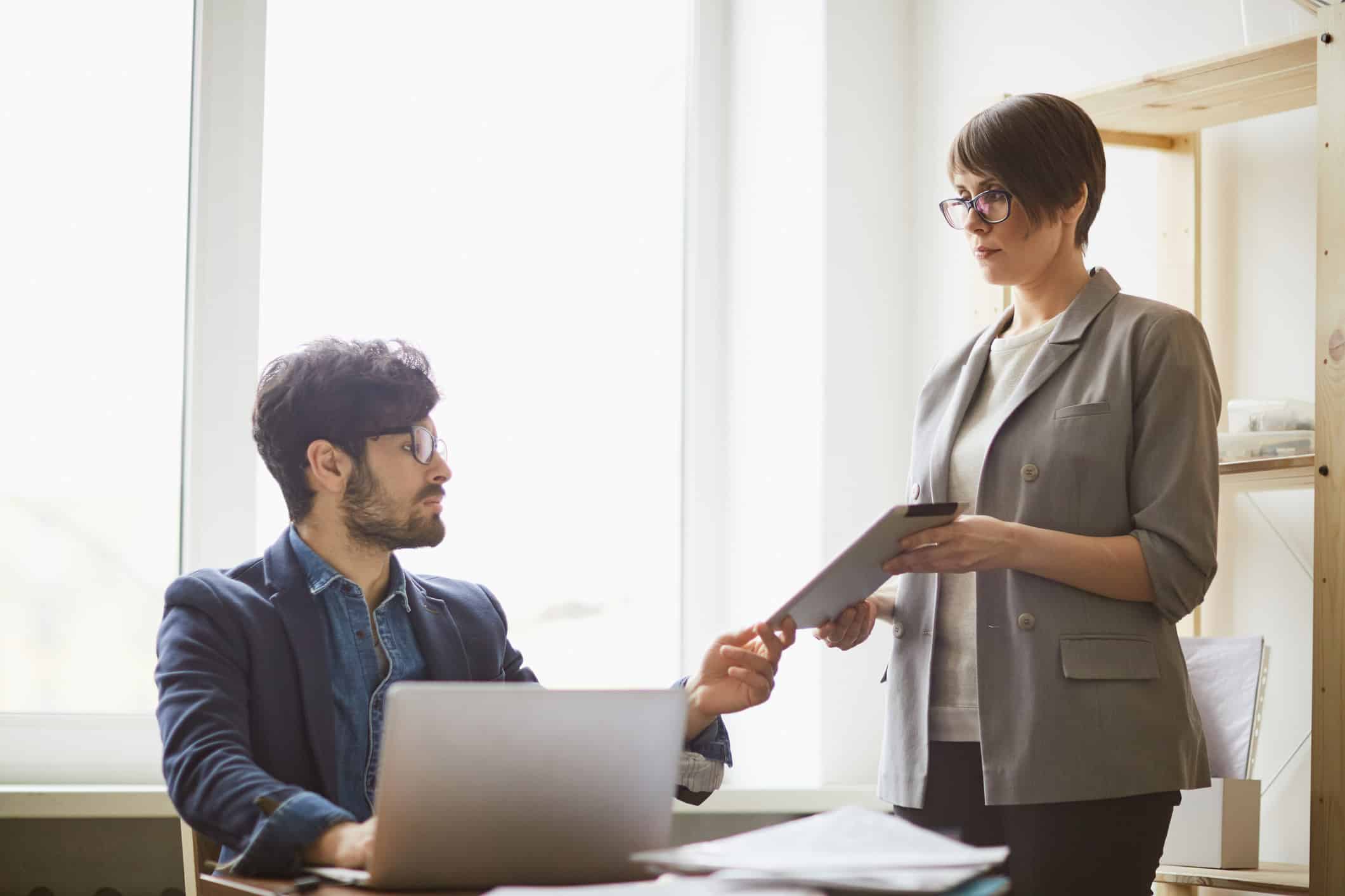 Woman hands a clipboard to man working on business valuation consulting services in an office.