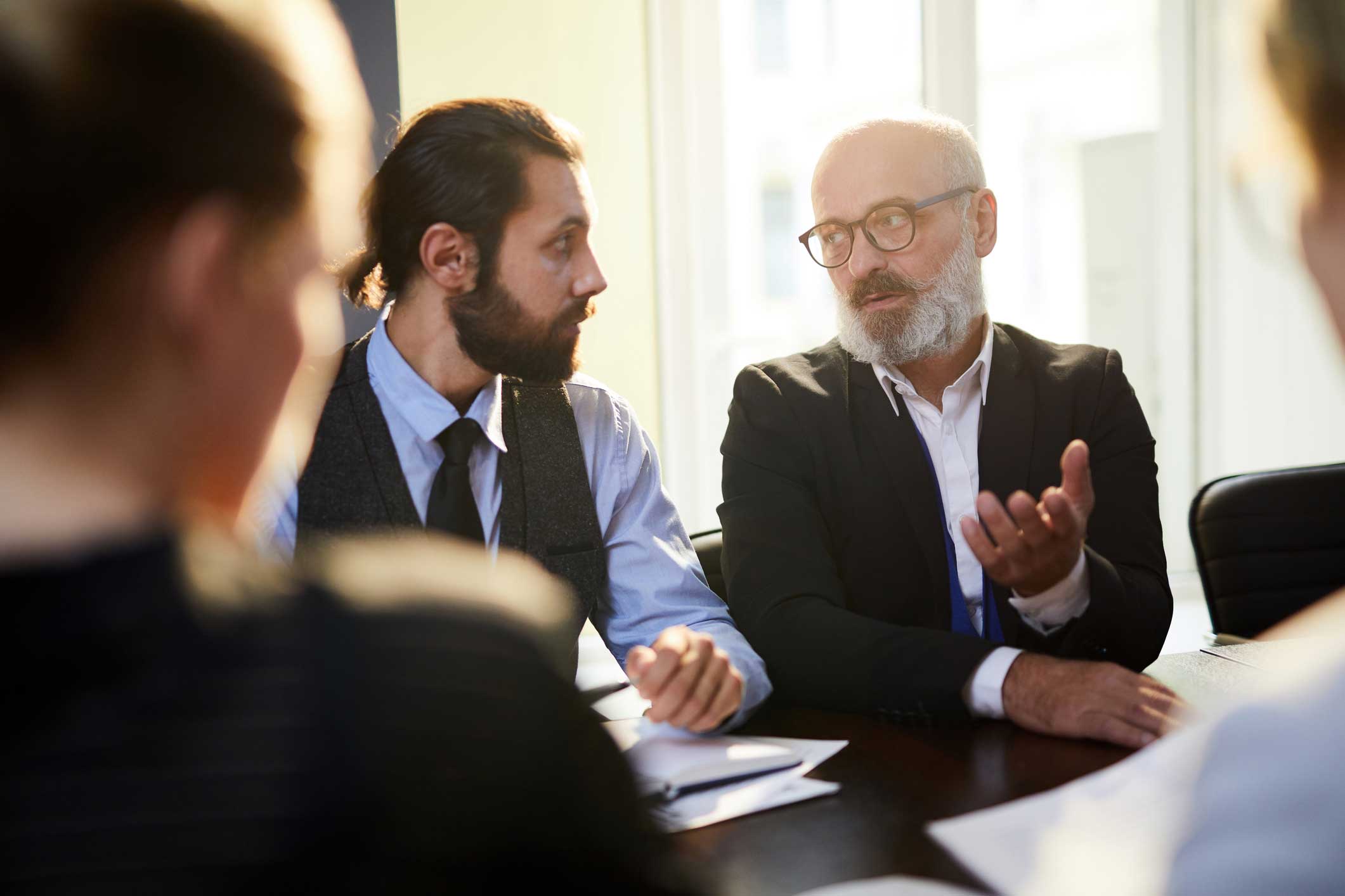 Two men in business attire discuss machine learning consulting at a meeting table.