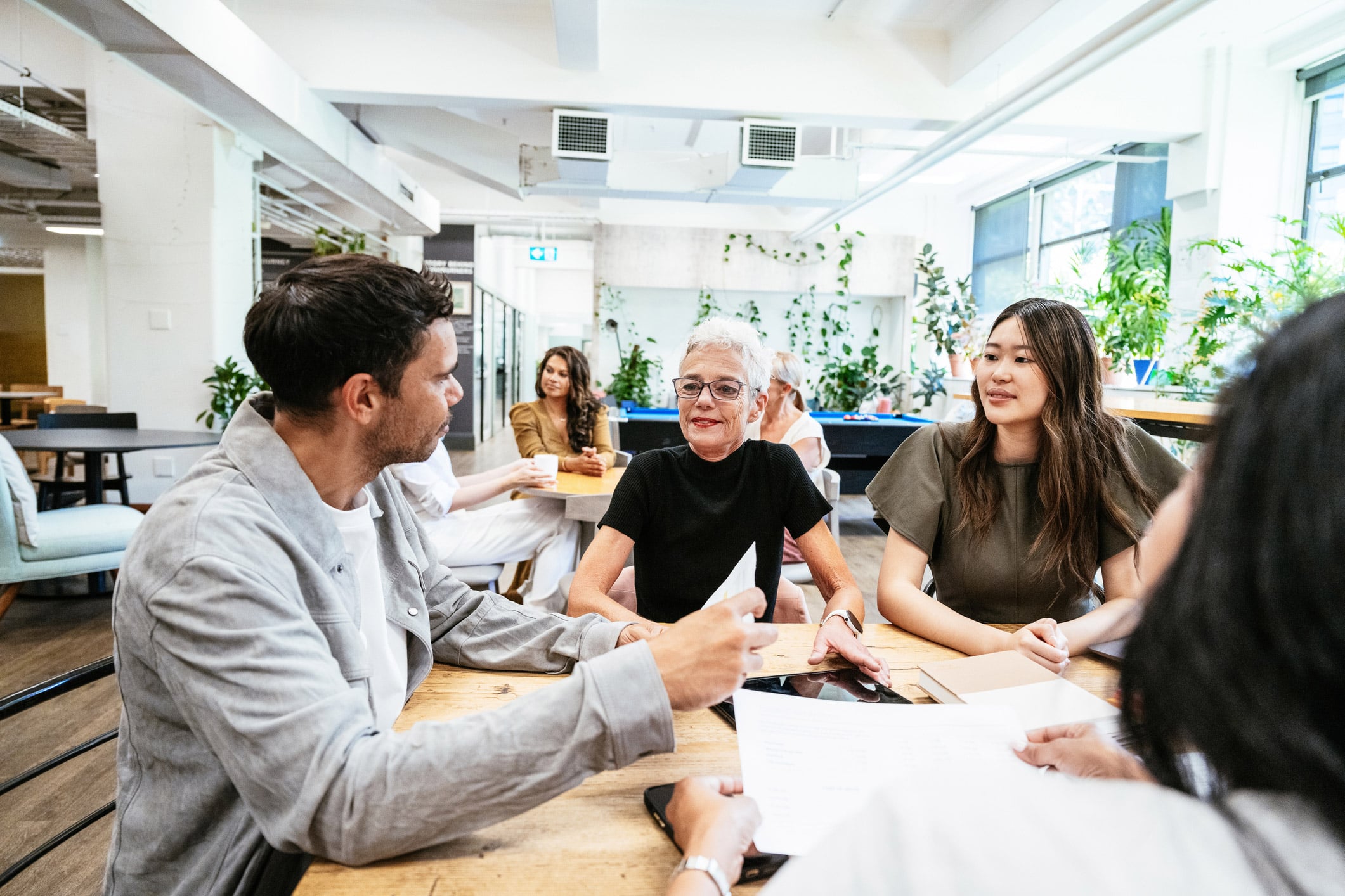 A diverse group discusses M&A Deal Structuring & Negotiation in a bright office meeting.