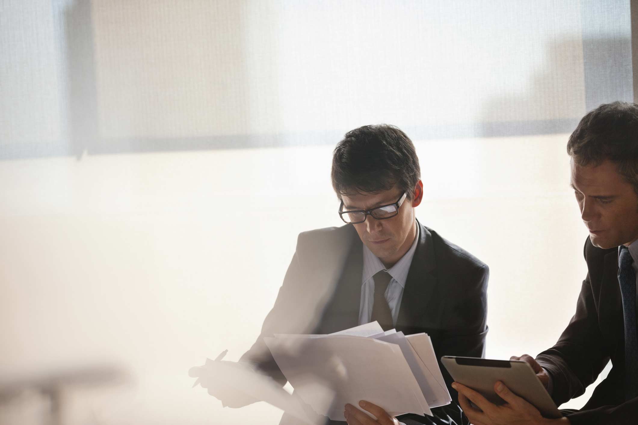 Two businessmen in suits review Advanced Analytics Advisory documents and a tablet in an office.