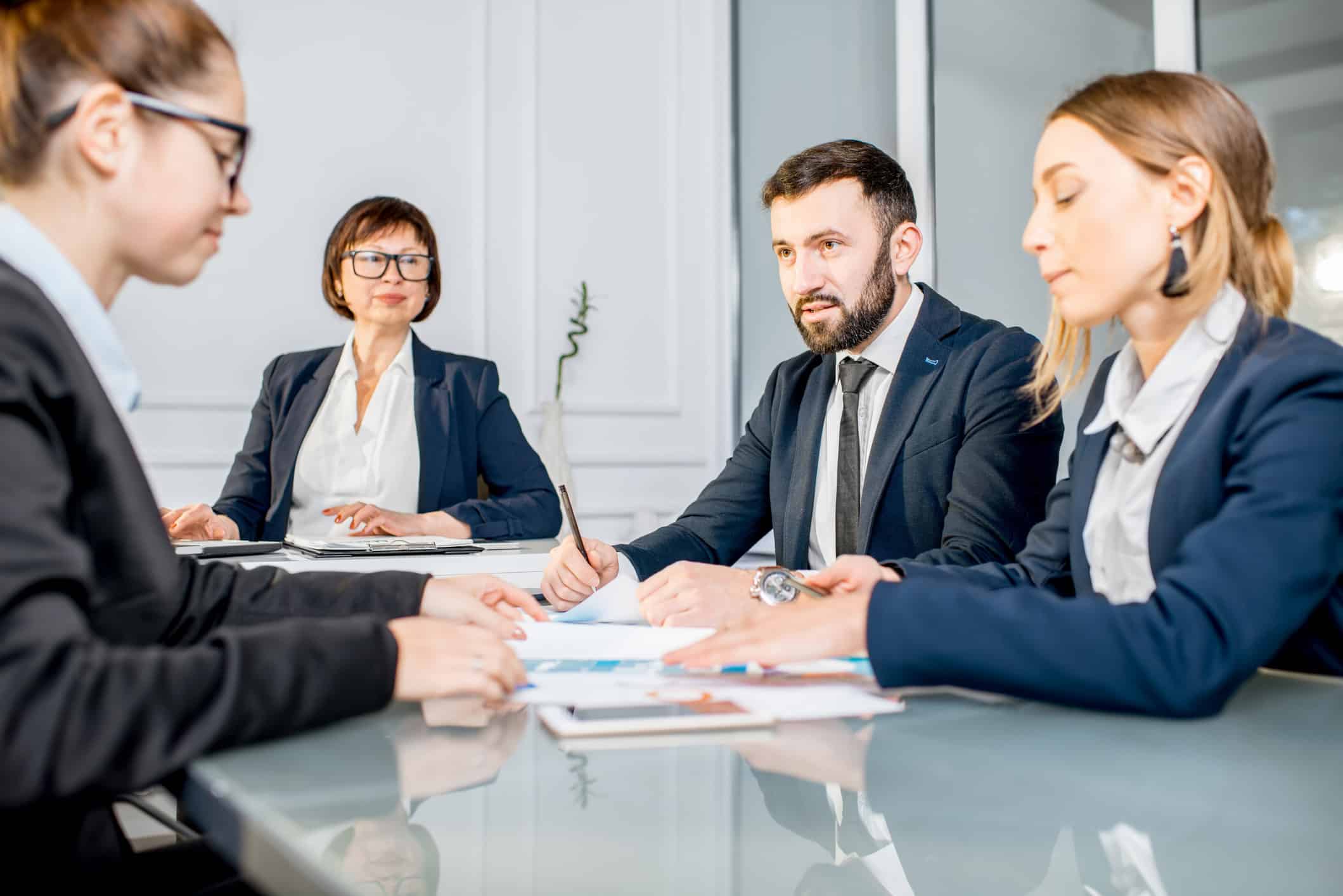 Four business professionals from a workforce development consulting firm meet around a glass table.
