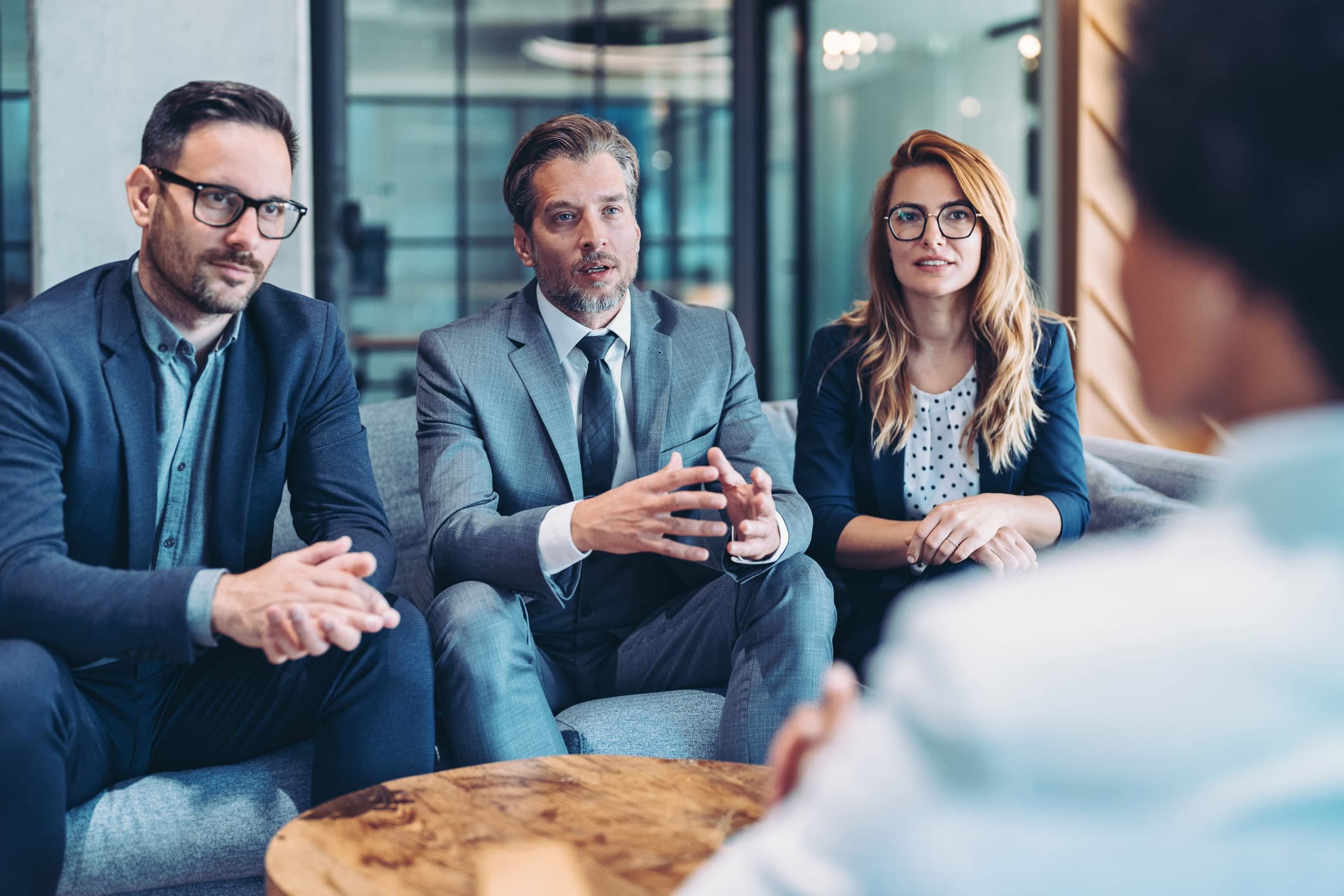 Three business professionals discuss M&A Due Diligence while seated on a couch.