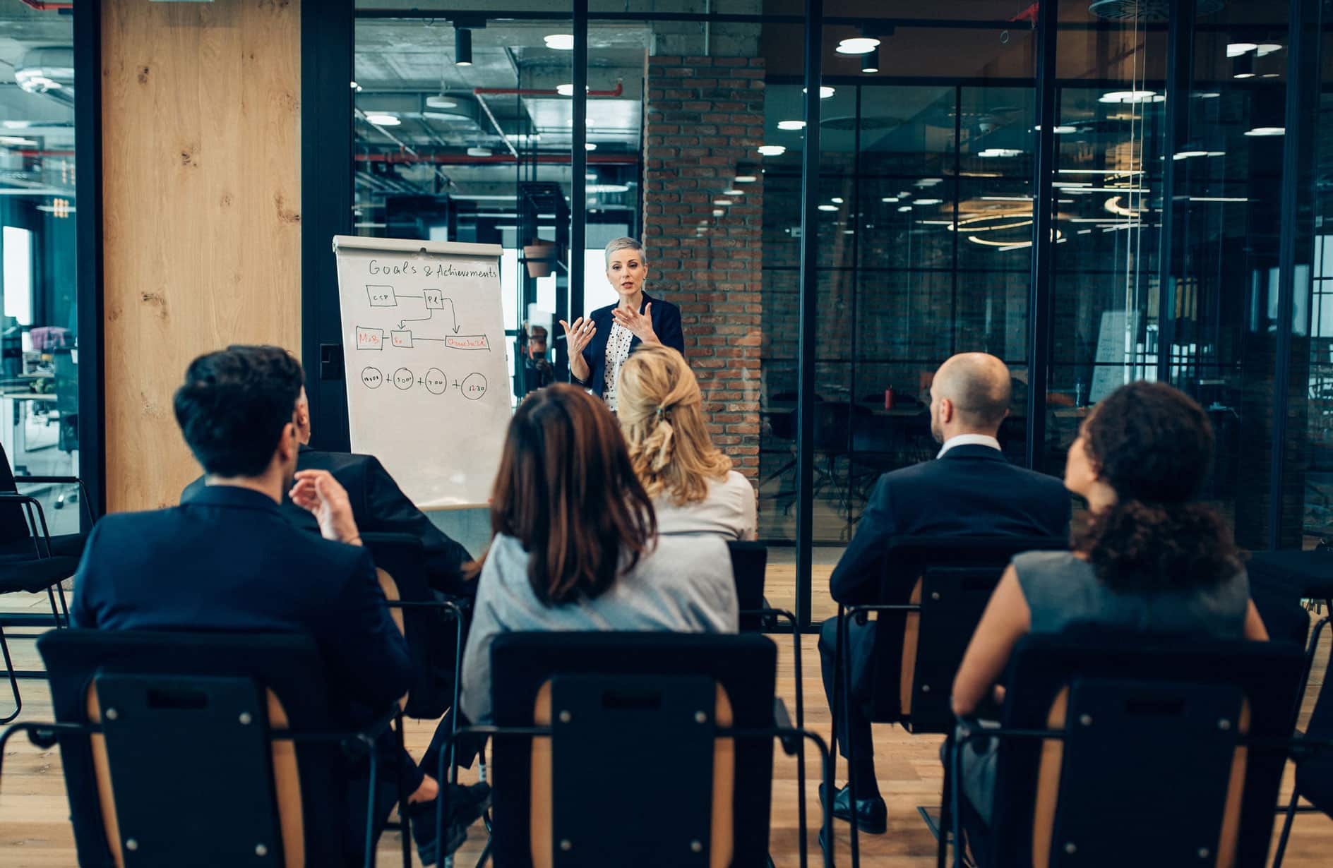 A woman leads a change management consulting presentation in a modern office with a whiteboard.
