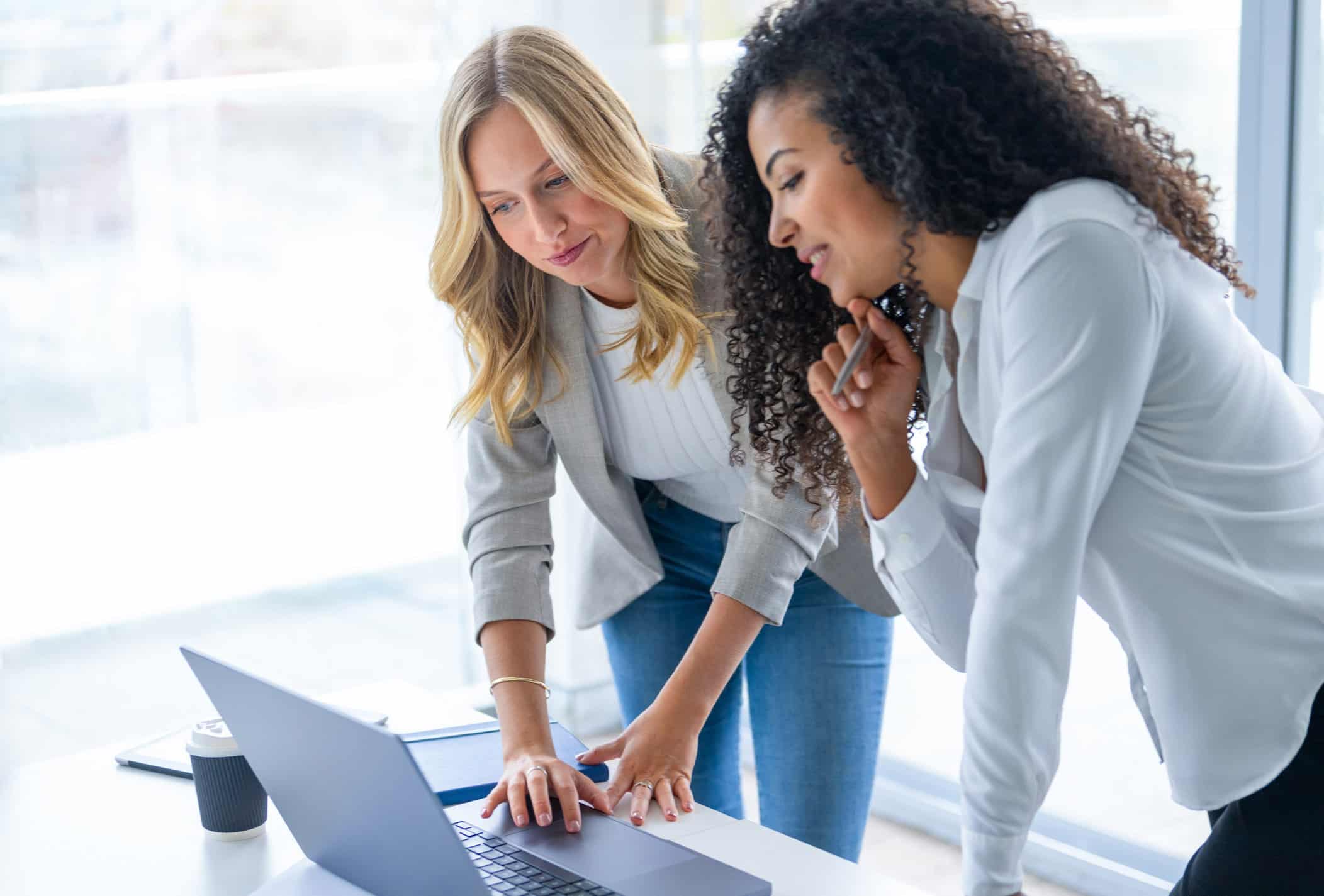 Two women in business attire discuss law firm strategic planning at a laptop in a bright office.