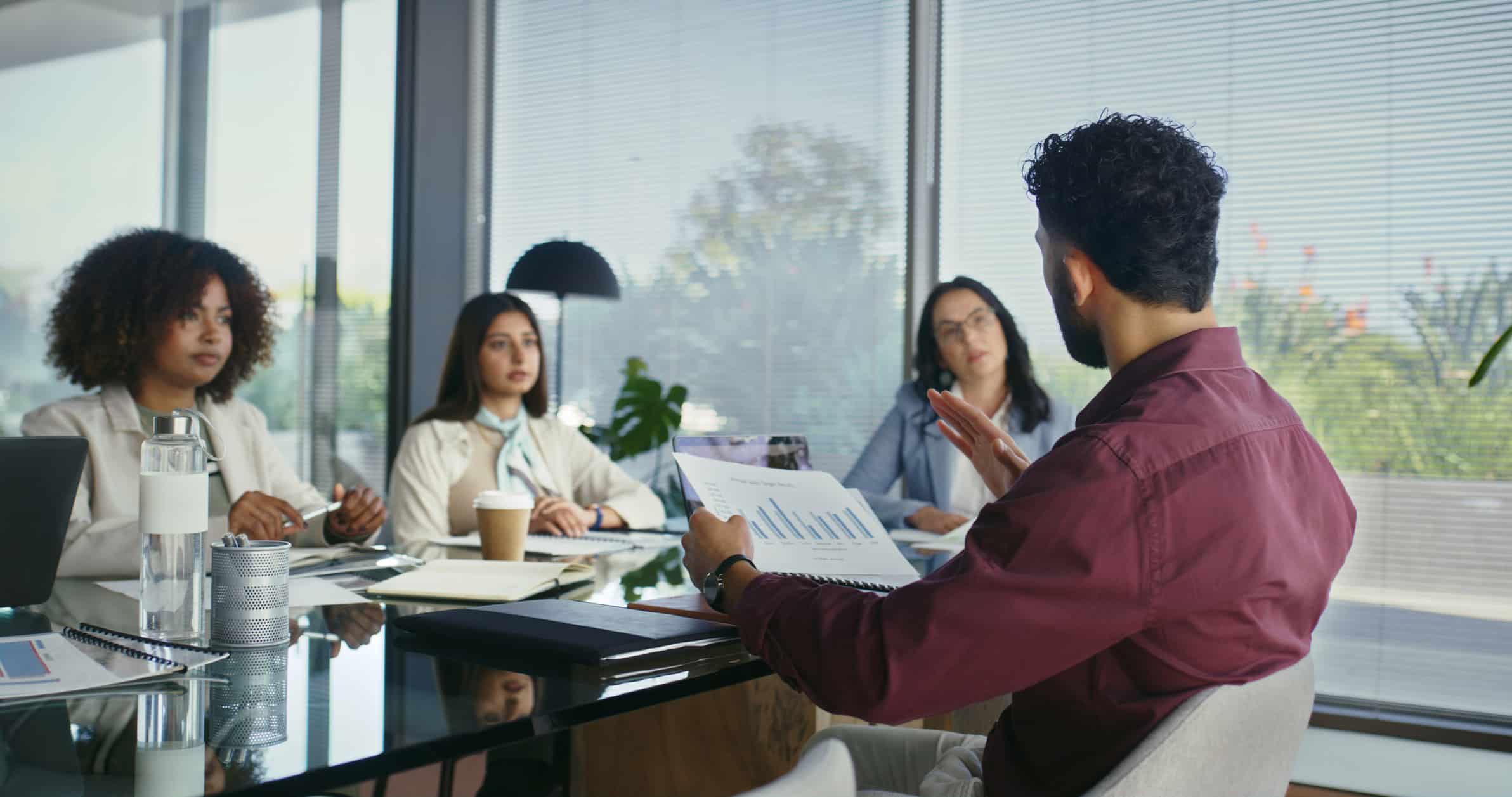 A man presents a Risk Management Planning chart to three colleagues in a modern office meeting room.