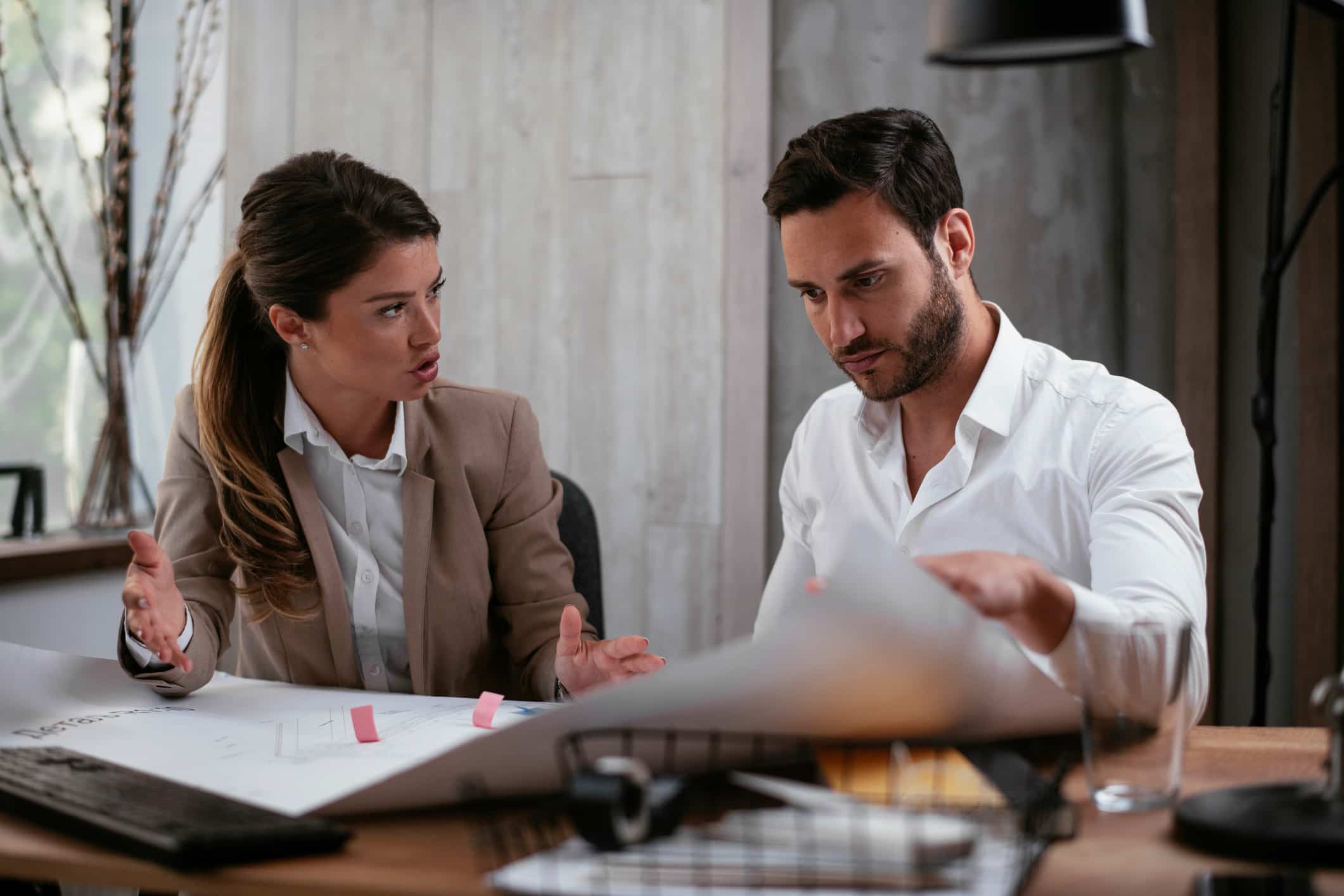 Two Technology-Assisted Review Consultants discuss documents seriously at an office desk.