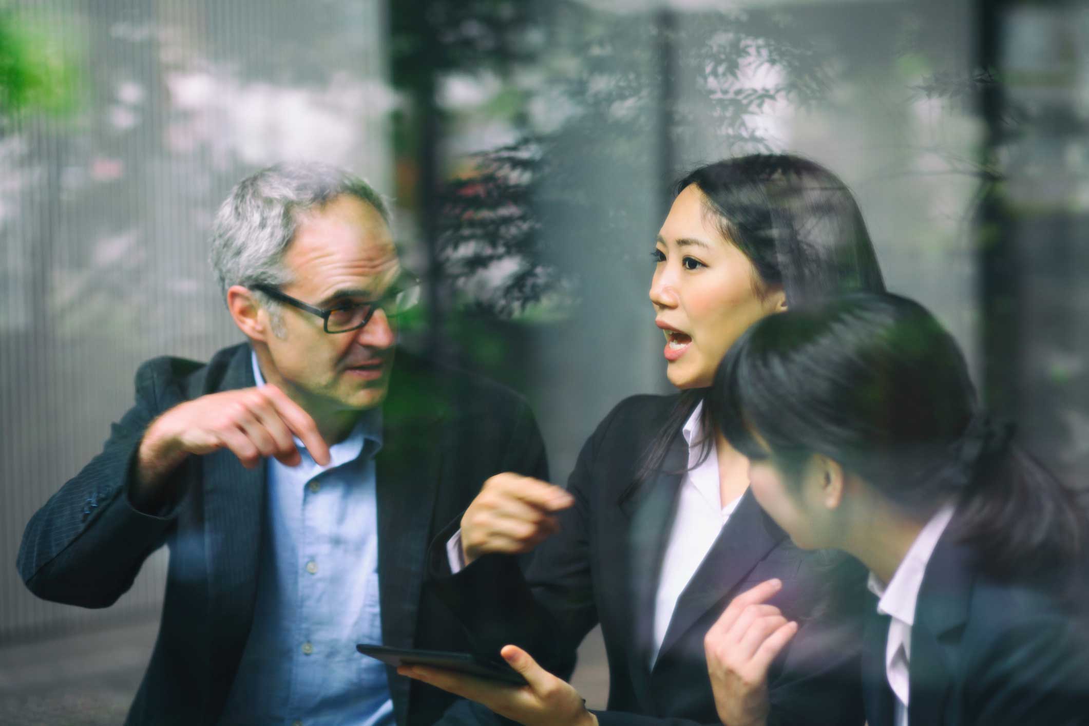 Three businesspeople discuss law firm expense management consulting through a glass window.