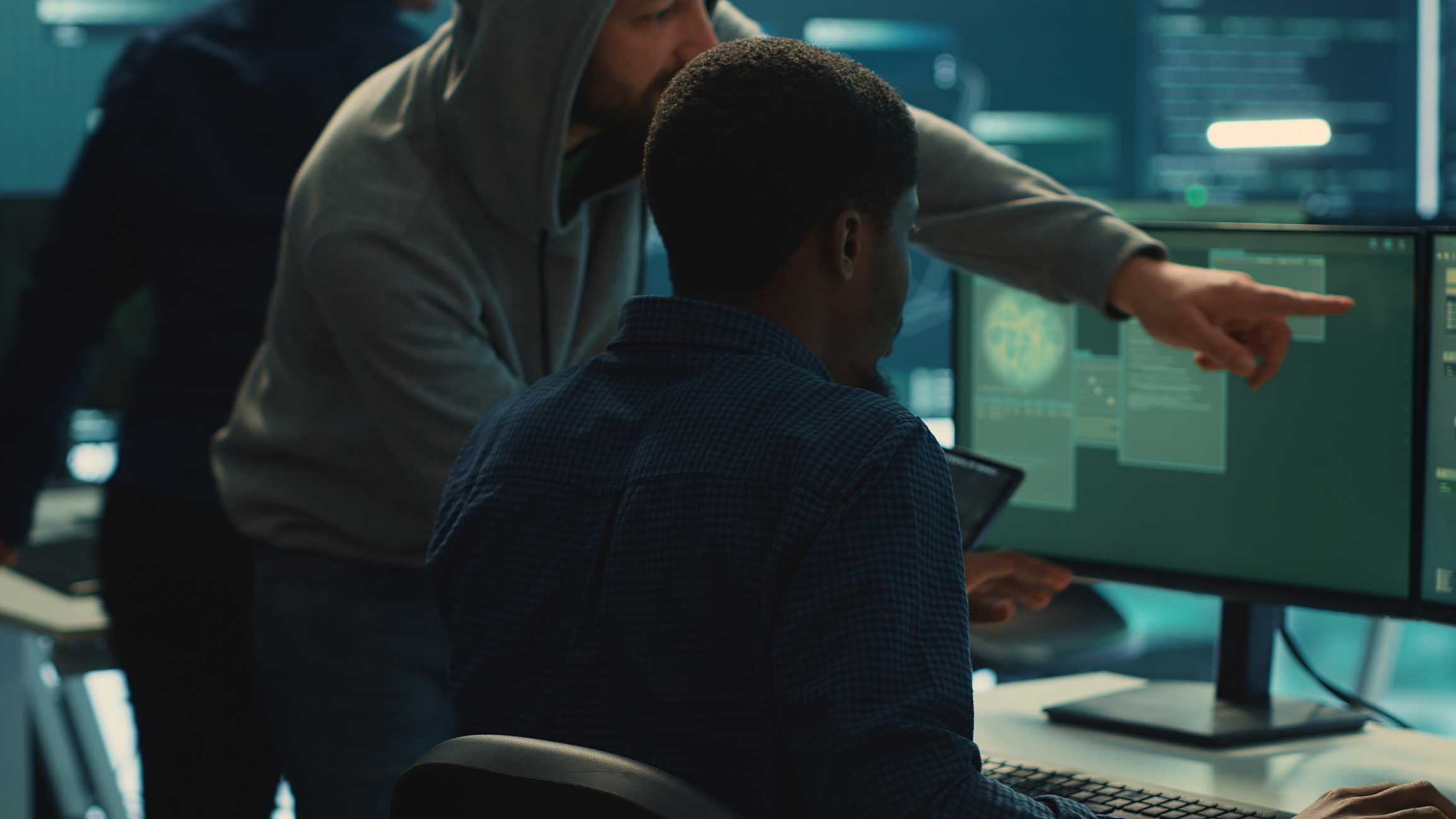 Two people reviewing code for IT disaster recovery consulting services in a dimly lit office.