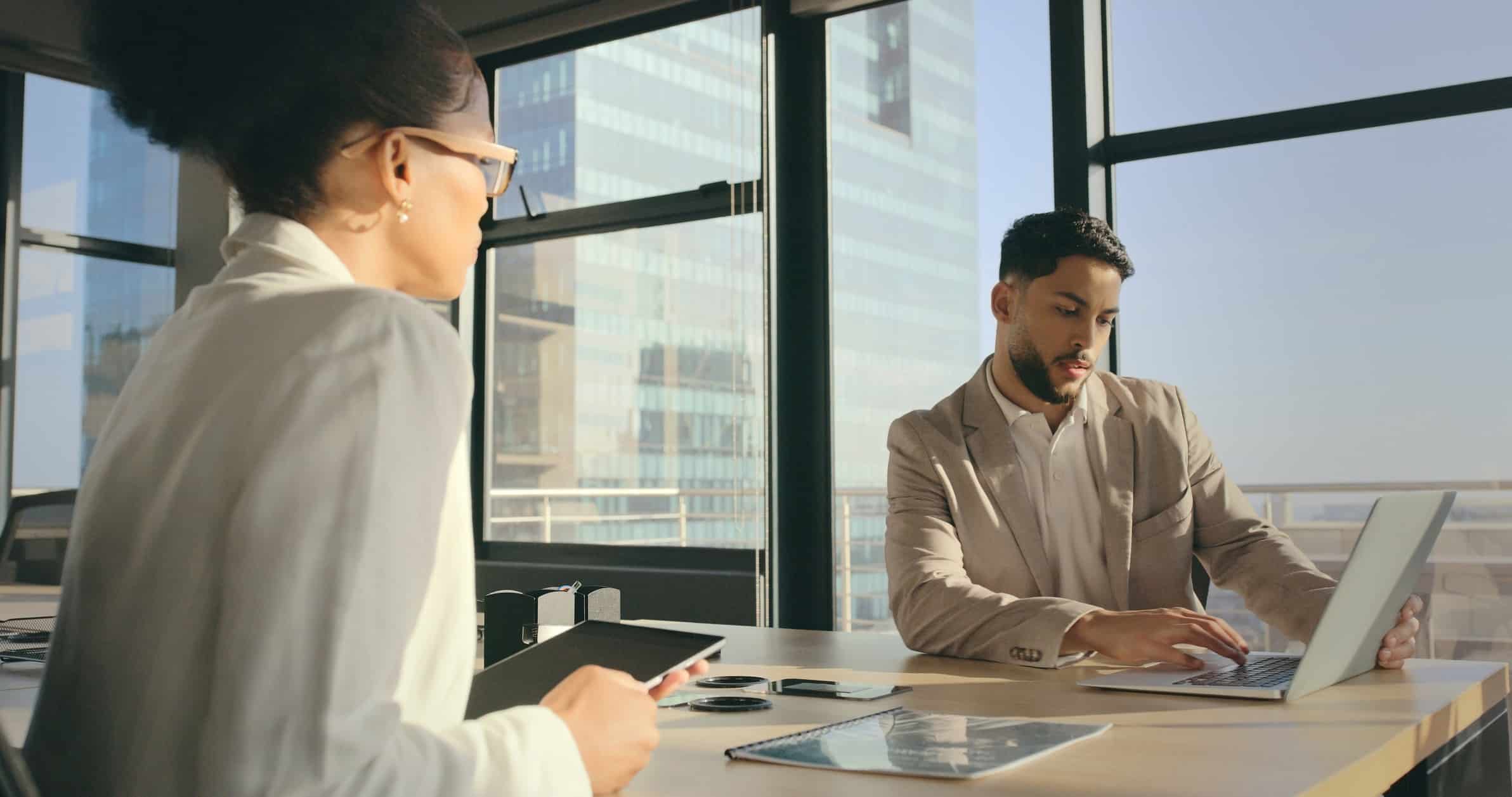 Two people in an office, one using a laptop for witness preparation, the other holding a tablet.