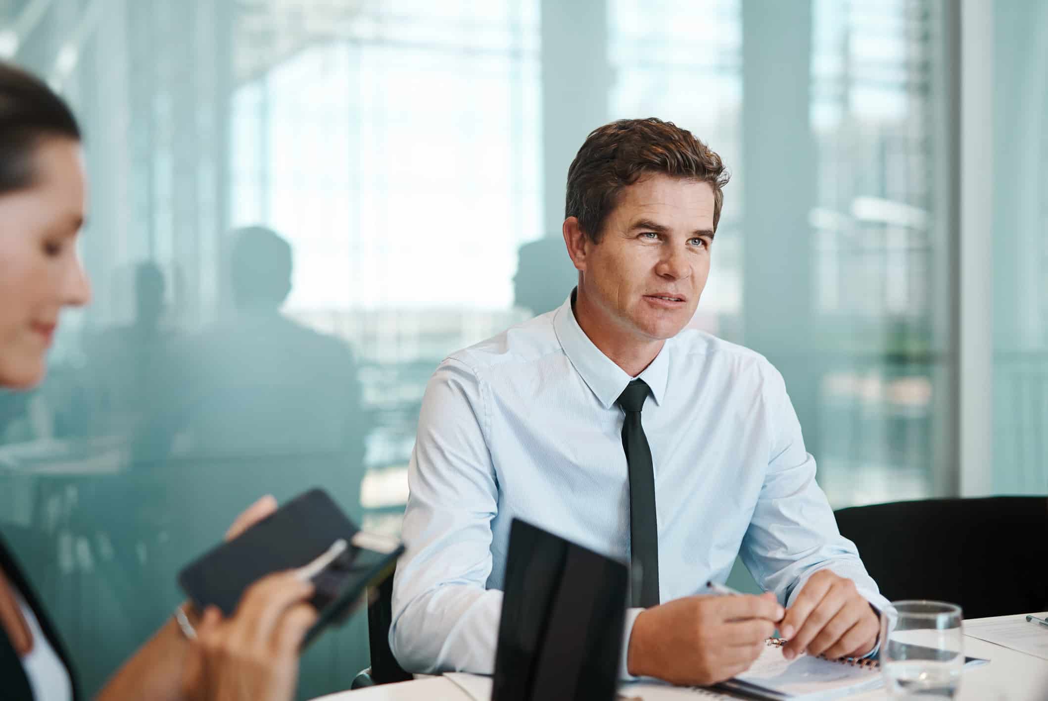 Man in business attire at a conference table, listening to a Business Valuation discussion.