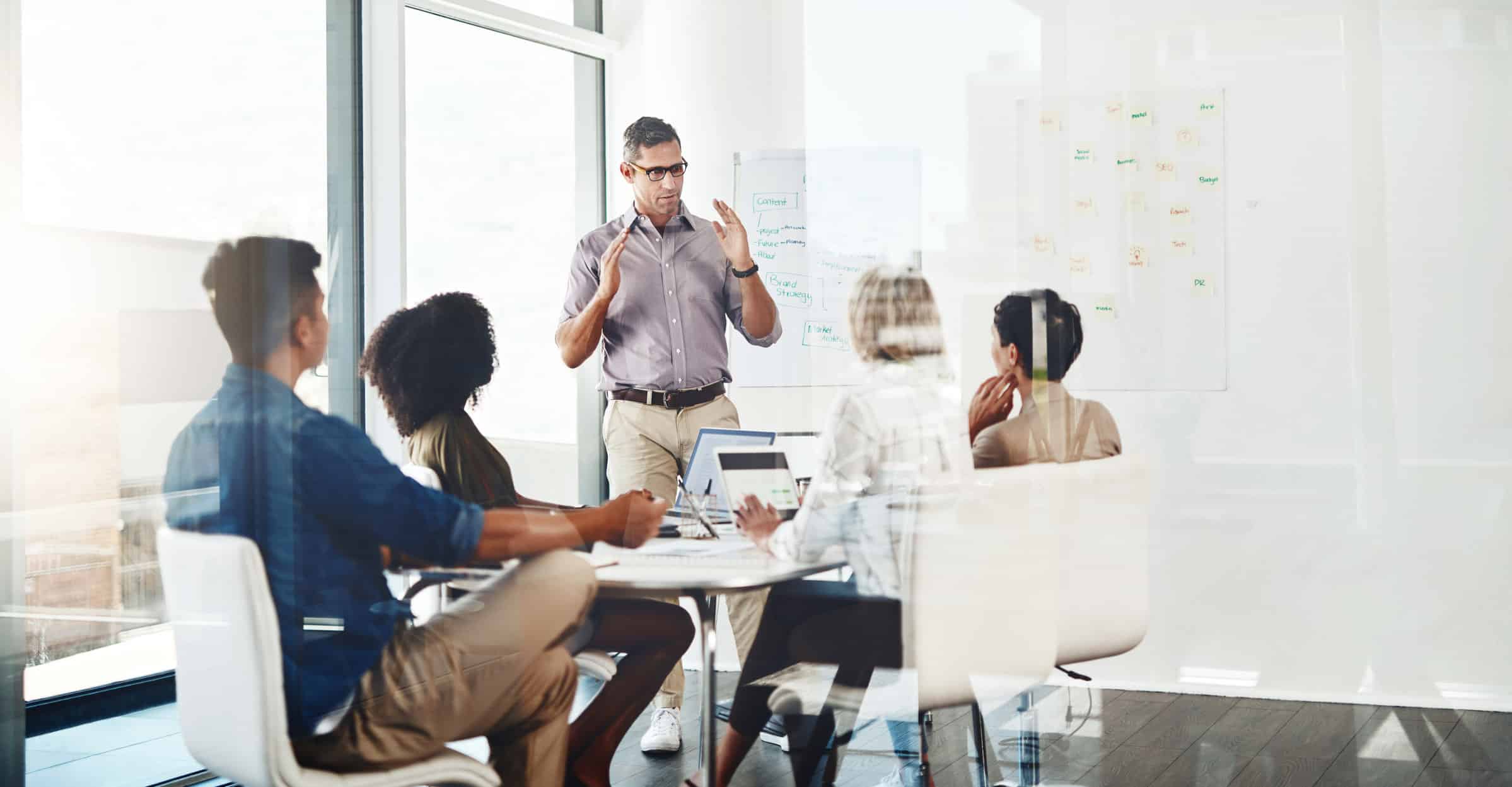 Man presenting Expense Reduction Execution to four colleagues in a bright, modern meeting room.
