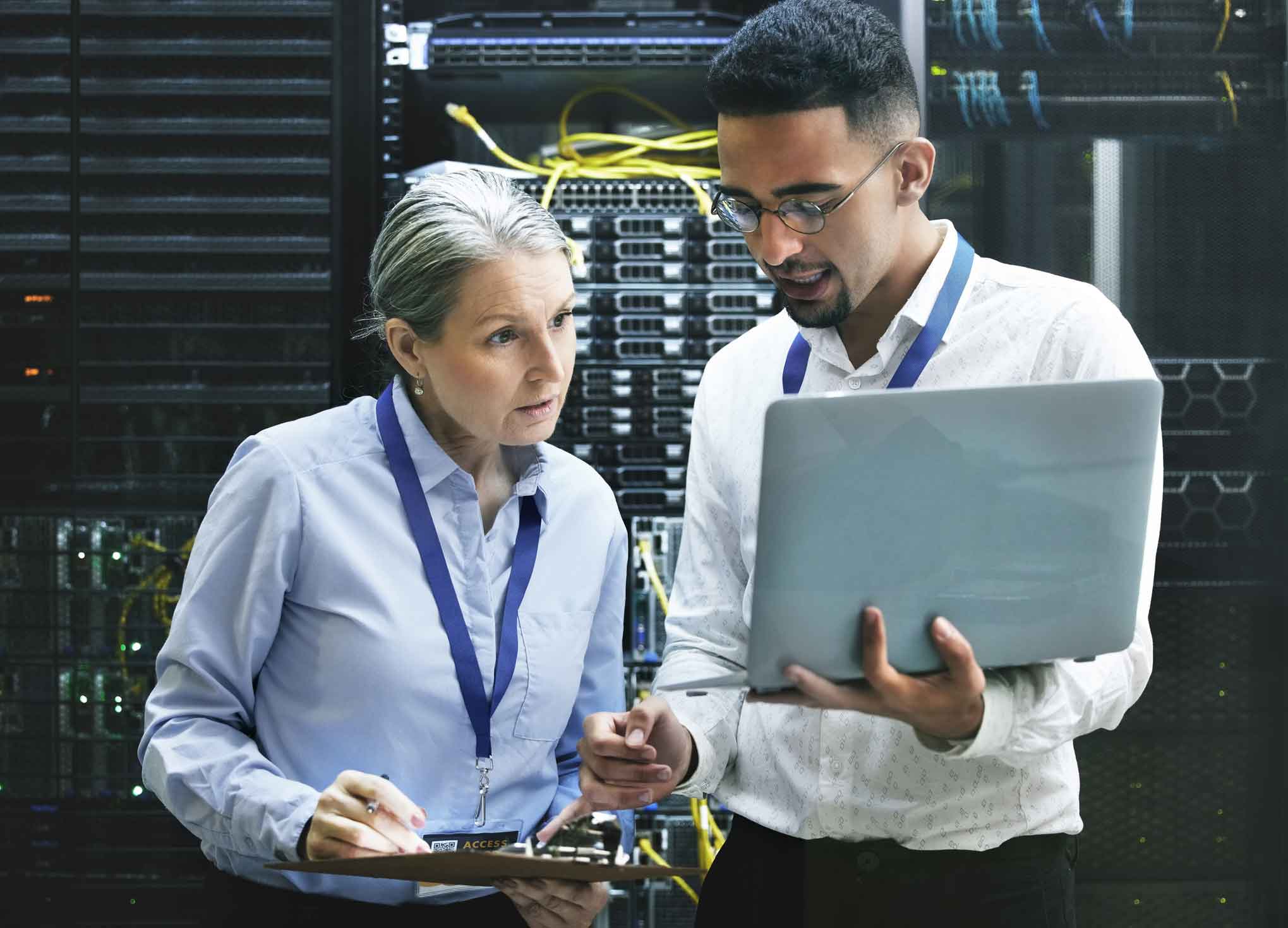 Two IT professionals discuss it disaster recovery execution in a server room with a laptop.