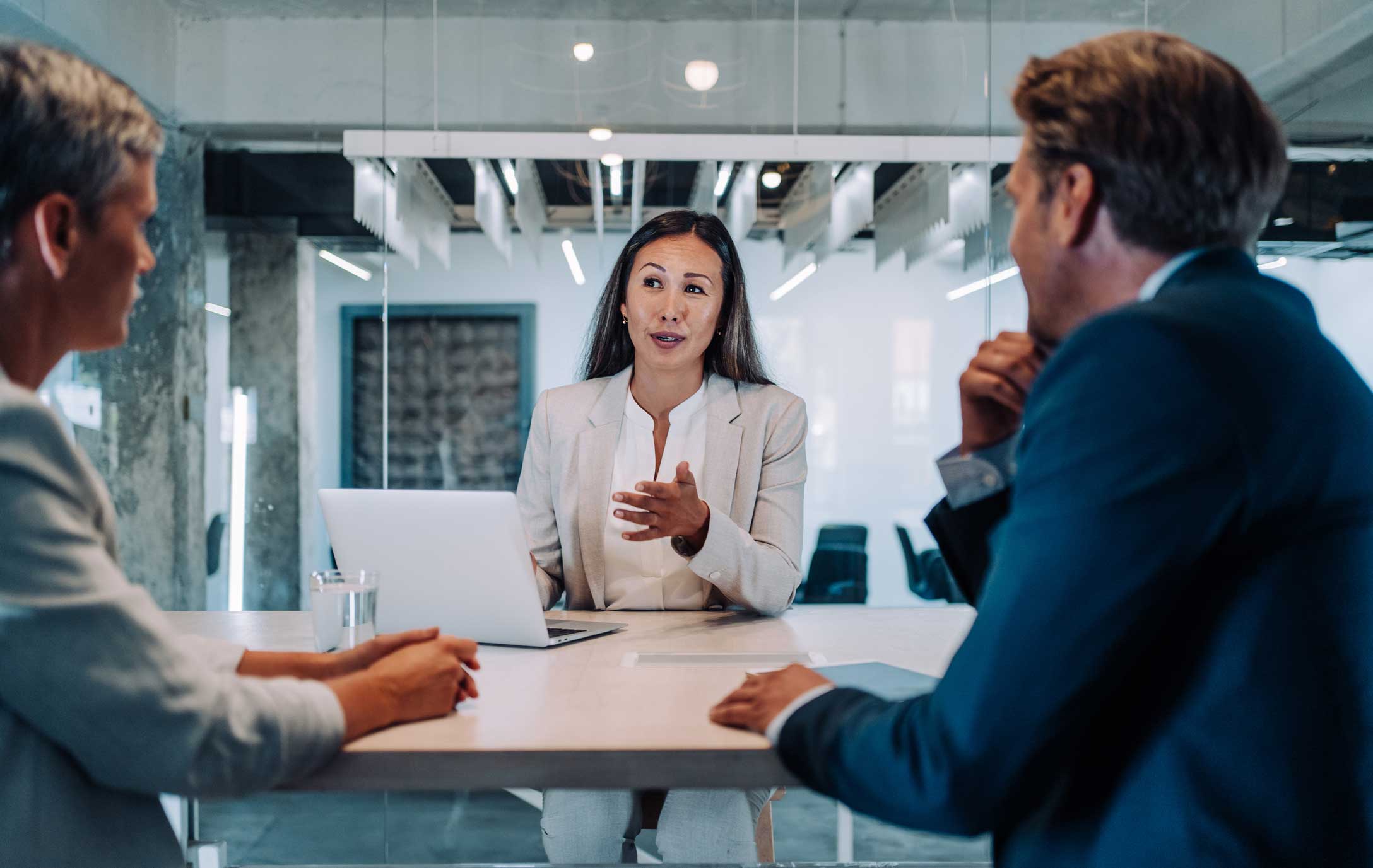 Three people discuss information security at a modern office table with a laptop.