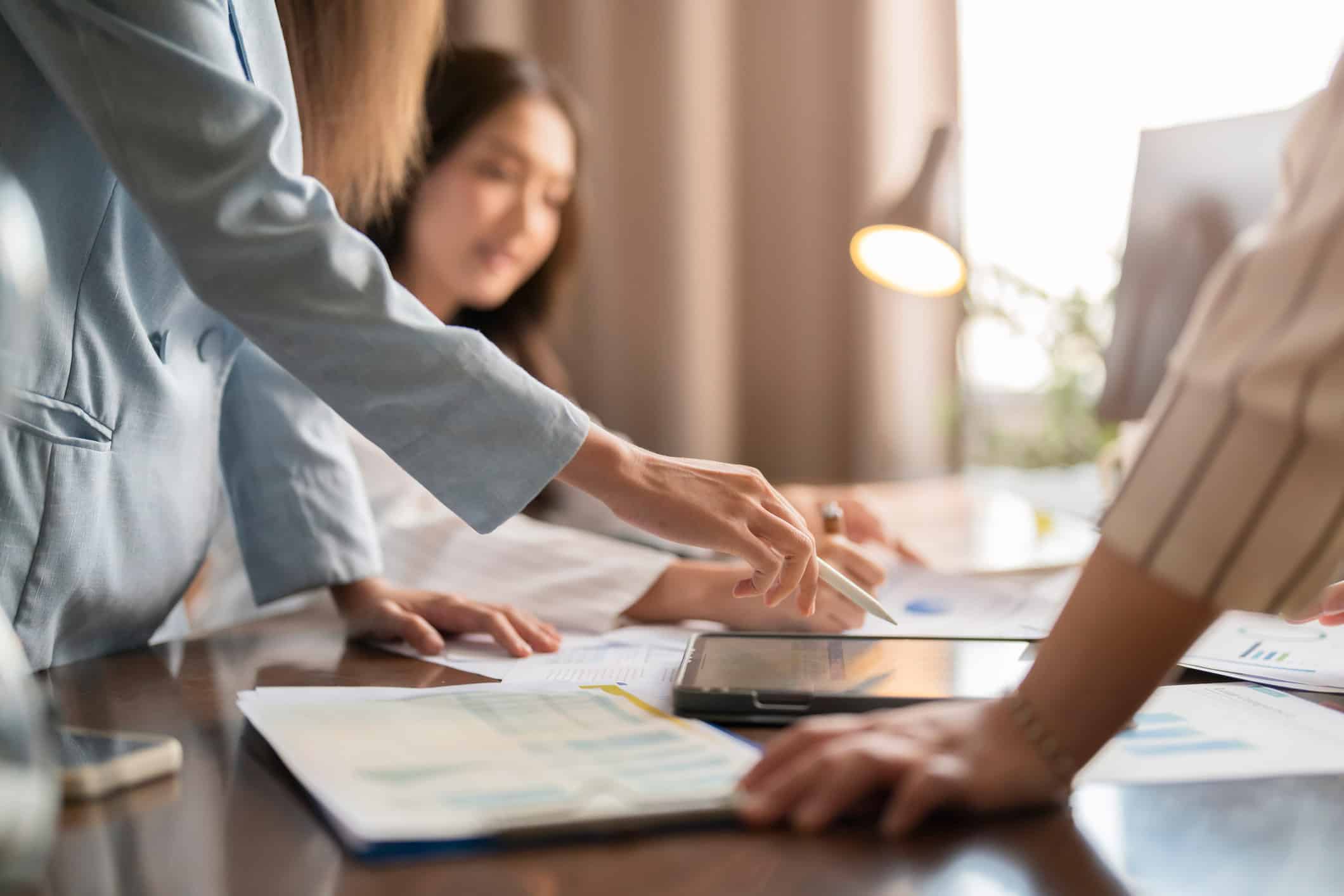Three people collaborating at a desk on papers and a tablet, focusing on Risk Management Execution.