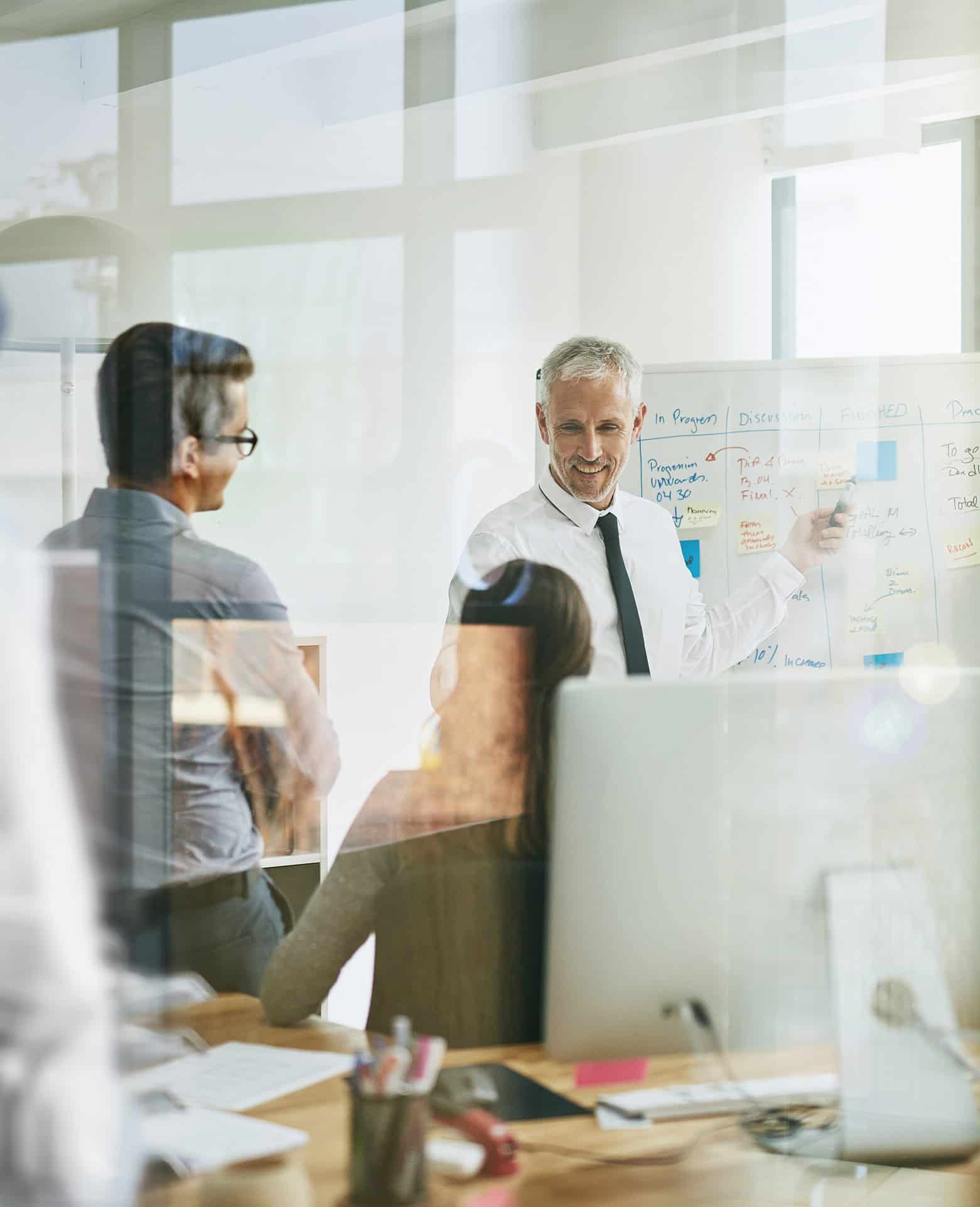 Smiling man presents law firm strategic planning execution at a whiteboard to colleagues.