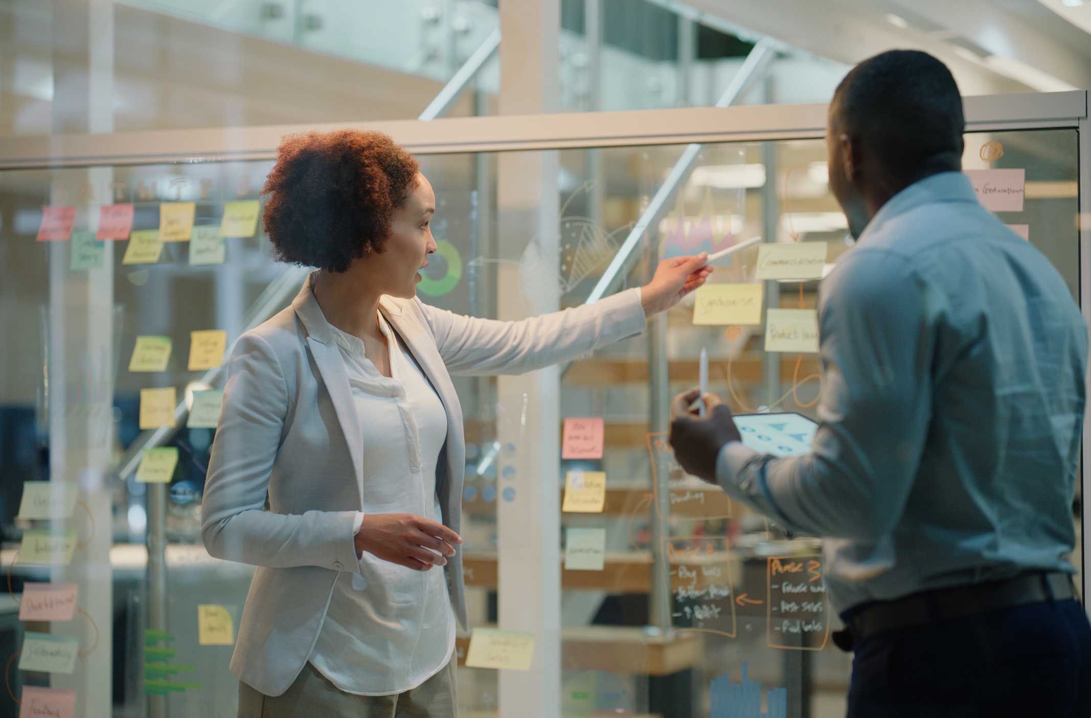 Two people discuss Cybersecurity Execution with notes on a glass wall in an office.