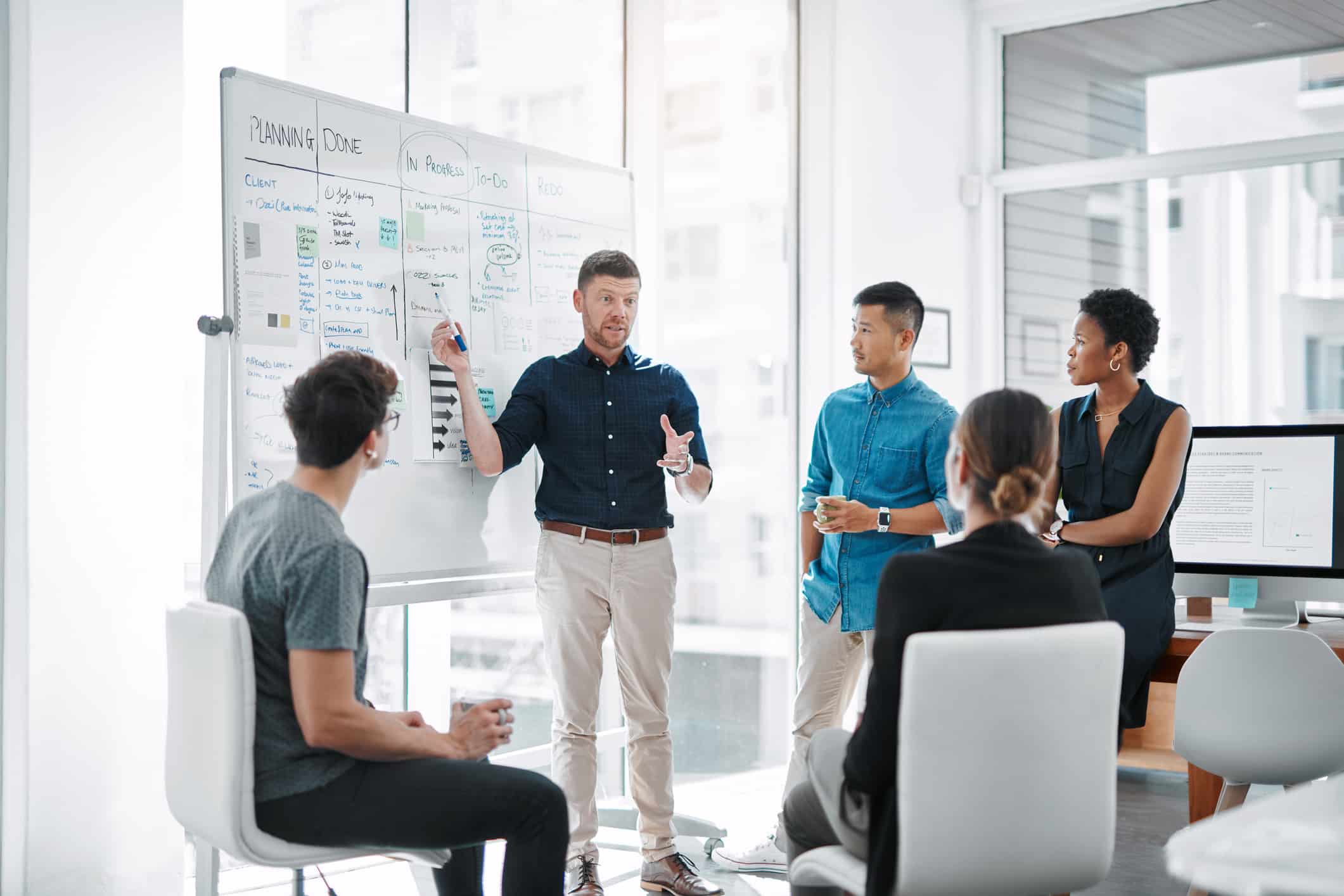 Man presenting Law Firm Growth Roadmaps on a whiteboard to four colleagues in a modern office.