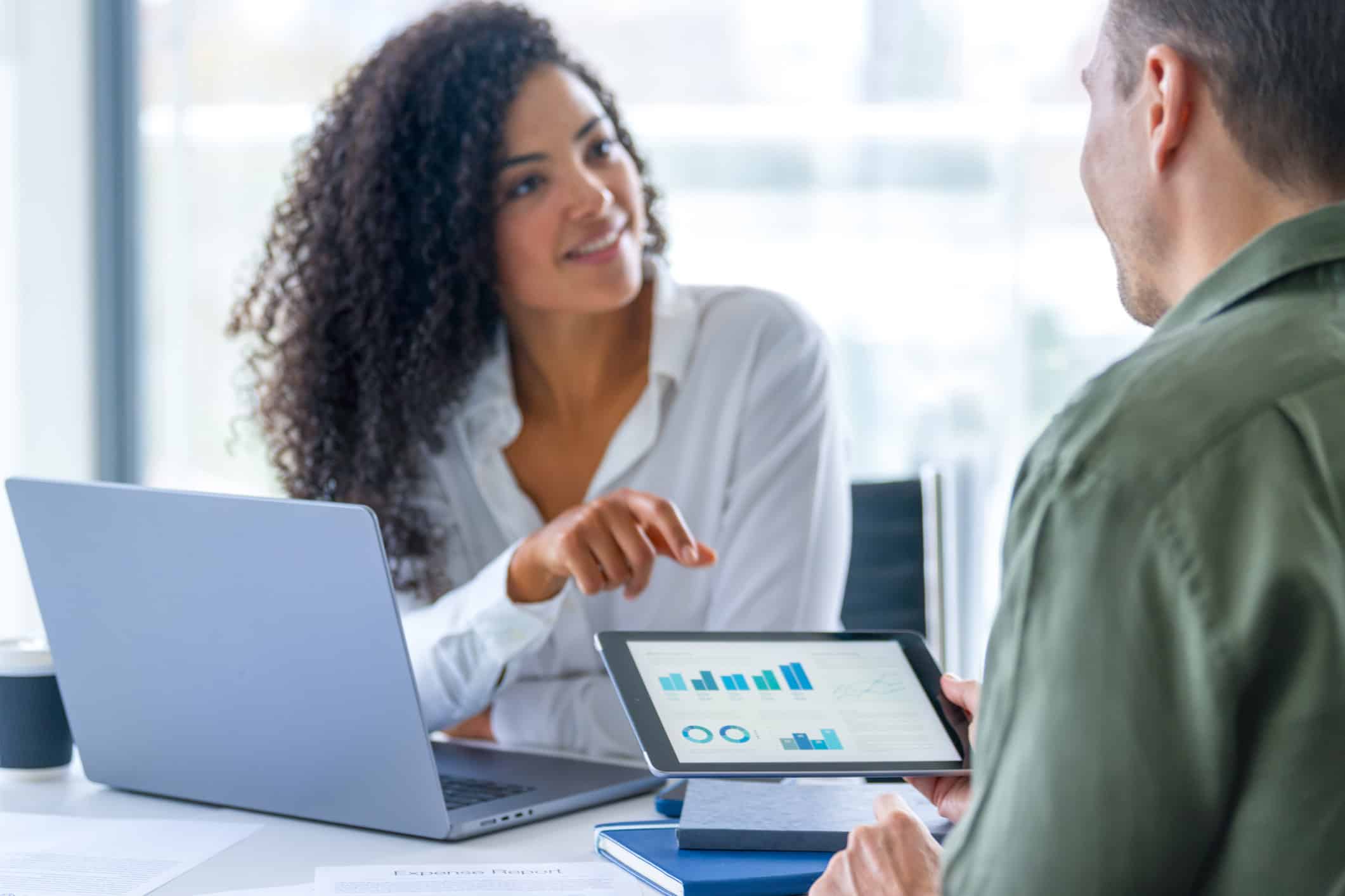 Two people discussing law firm strategic planning KPIs on a tablet at a desk with a laptop.
