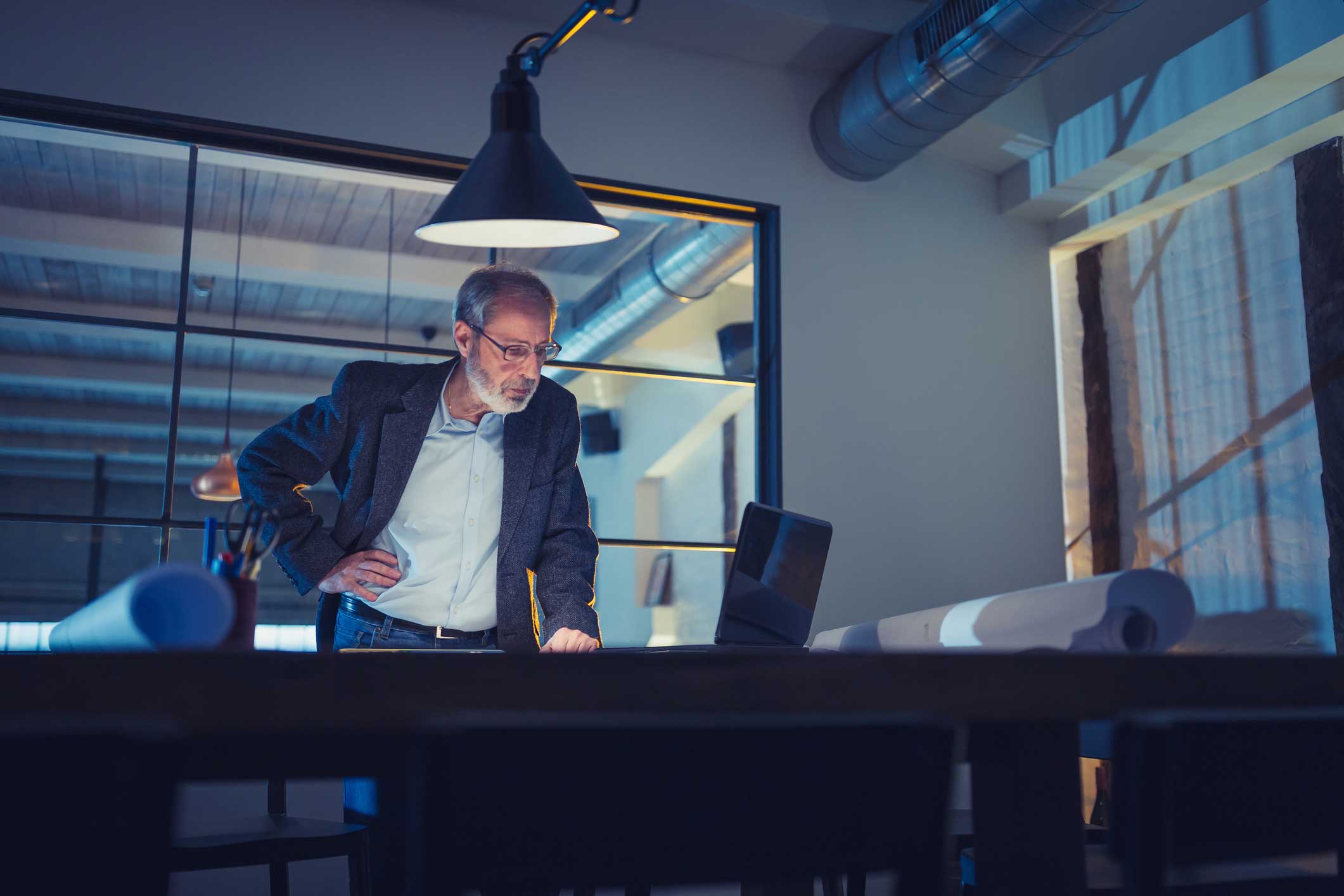 Older man in an office reviews documents on cybersecurity compliance consulting under a lamp.