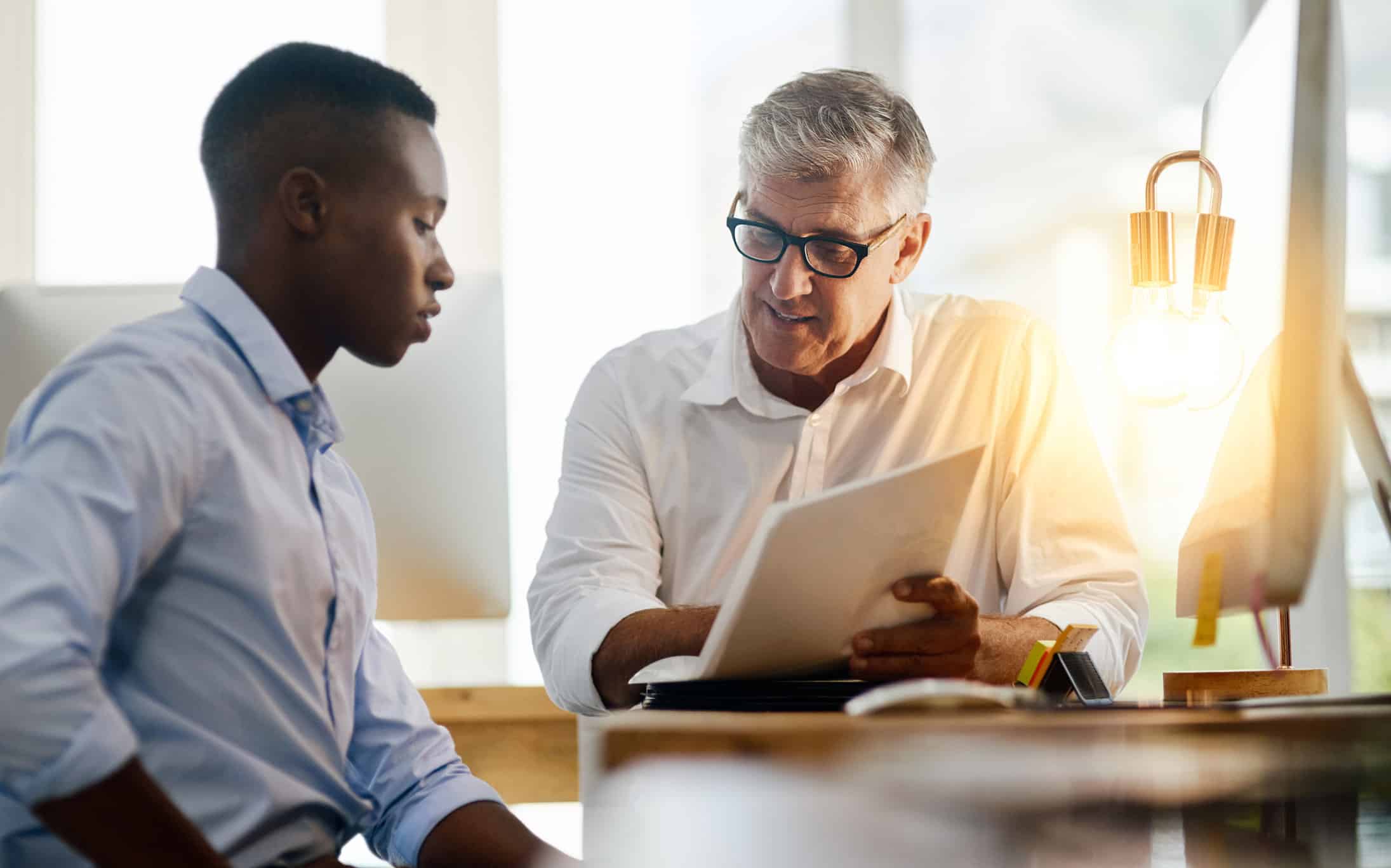 Older man showing a Forensic Litigation document to a younger man in a bright office setting.