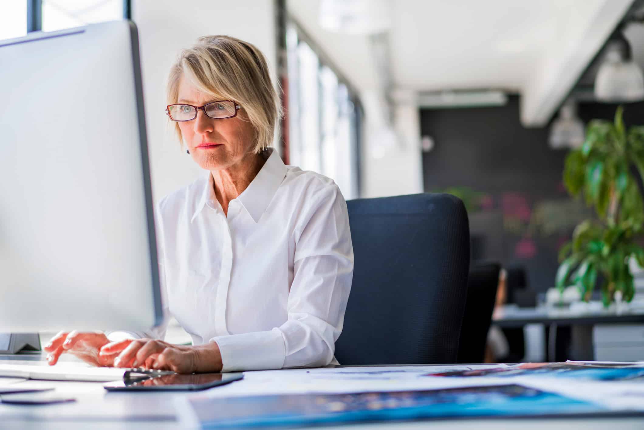 Woman with glasses developing case strategy at a computer in a bright modern office.