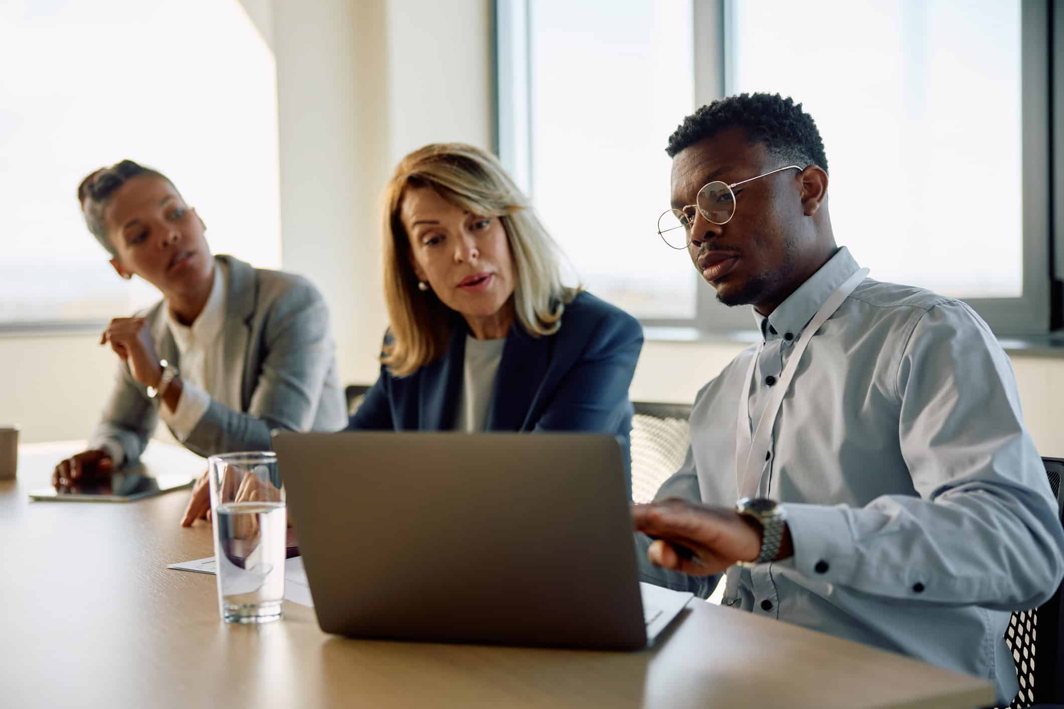 Three people in business attire discuss Business Valuation at a conference table with a laptop.