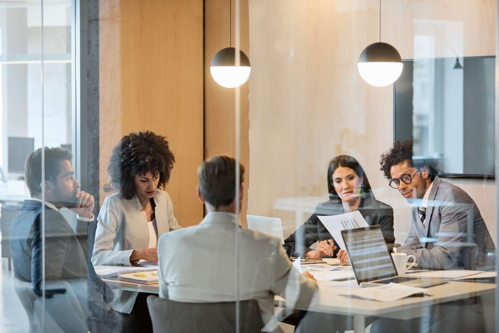 Five change management consultants meet in business attire around a table in a glass office.