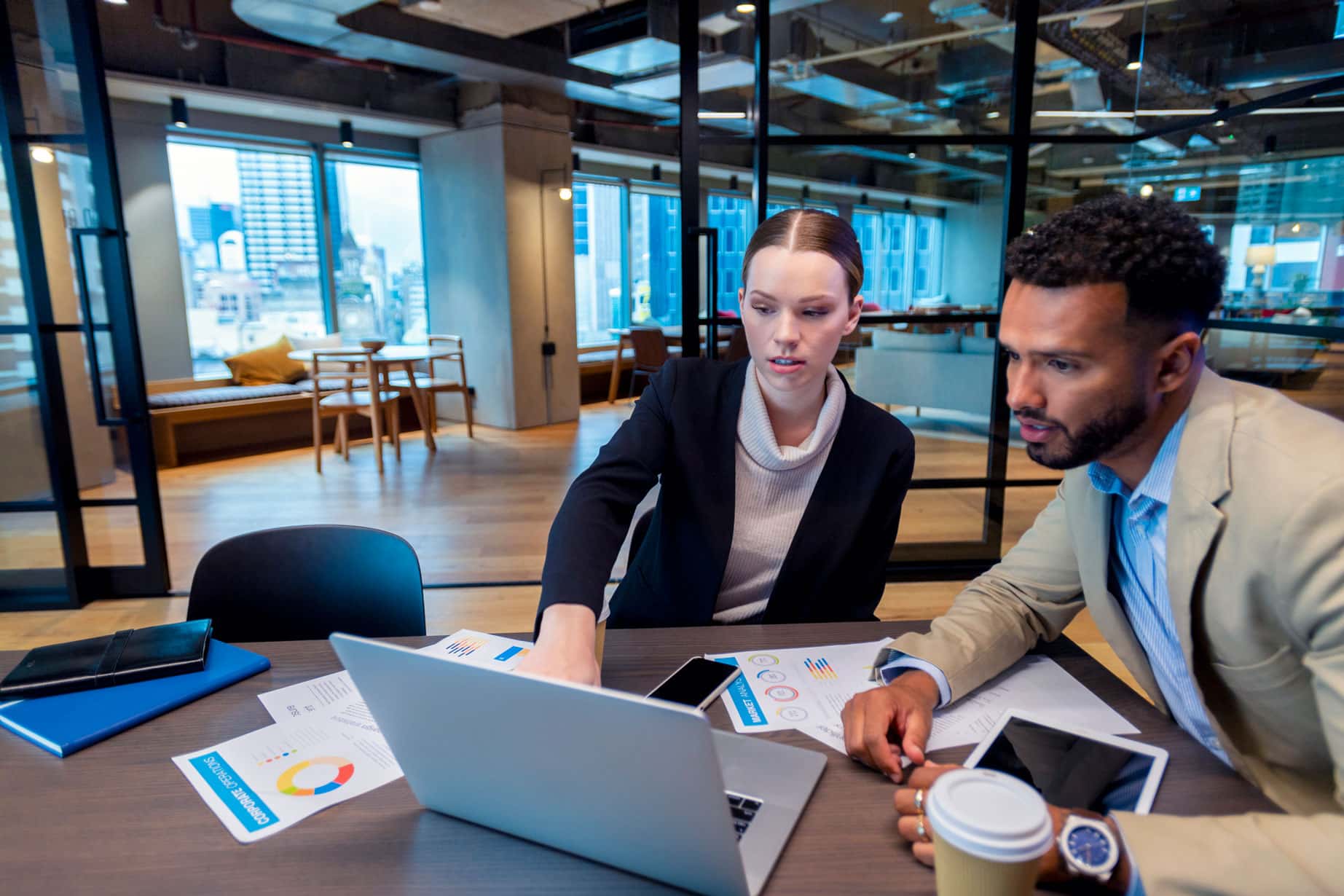 Two colleagues discuss charts on a laptop during a Business Intelligence Consulting session.