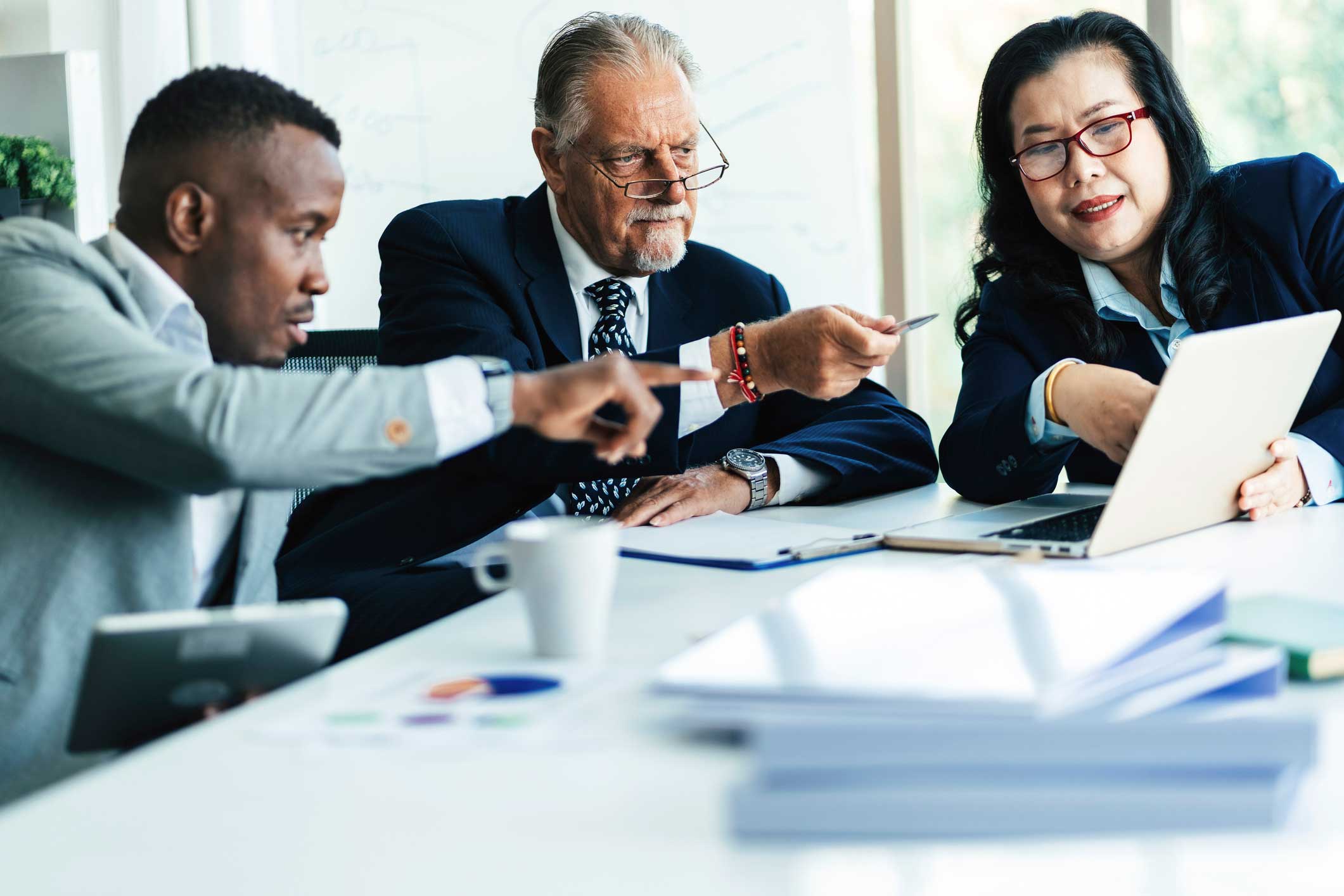 Three Law Firm Financial Management Consultants discuss strategy on a laptop in a meeting room.