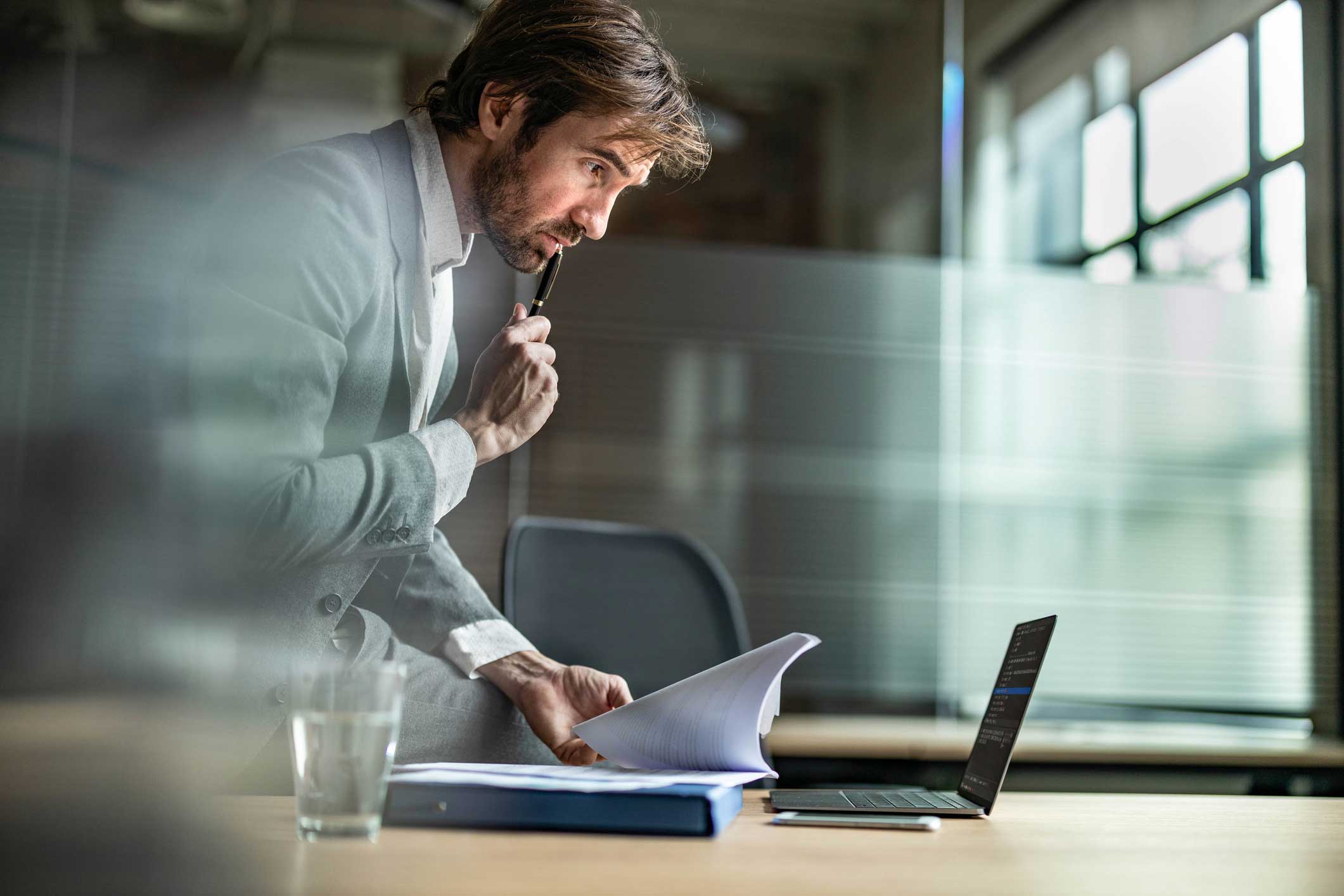 Man in suit reviewing cybersecurity compliance advisory documents on laptop in an office.