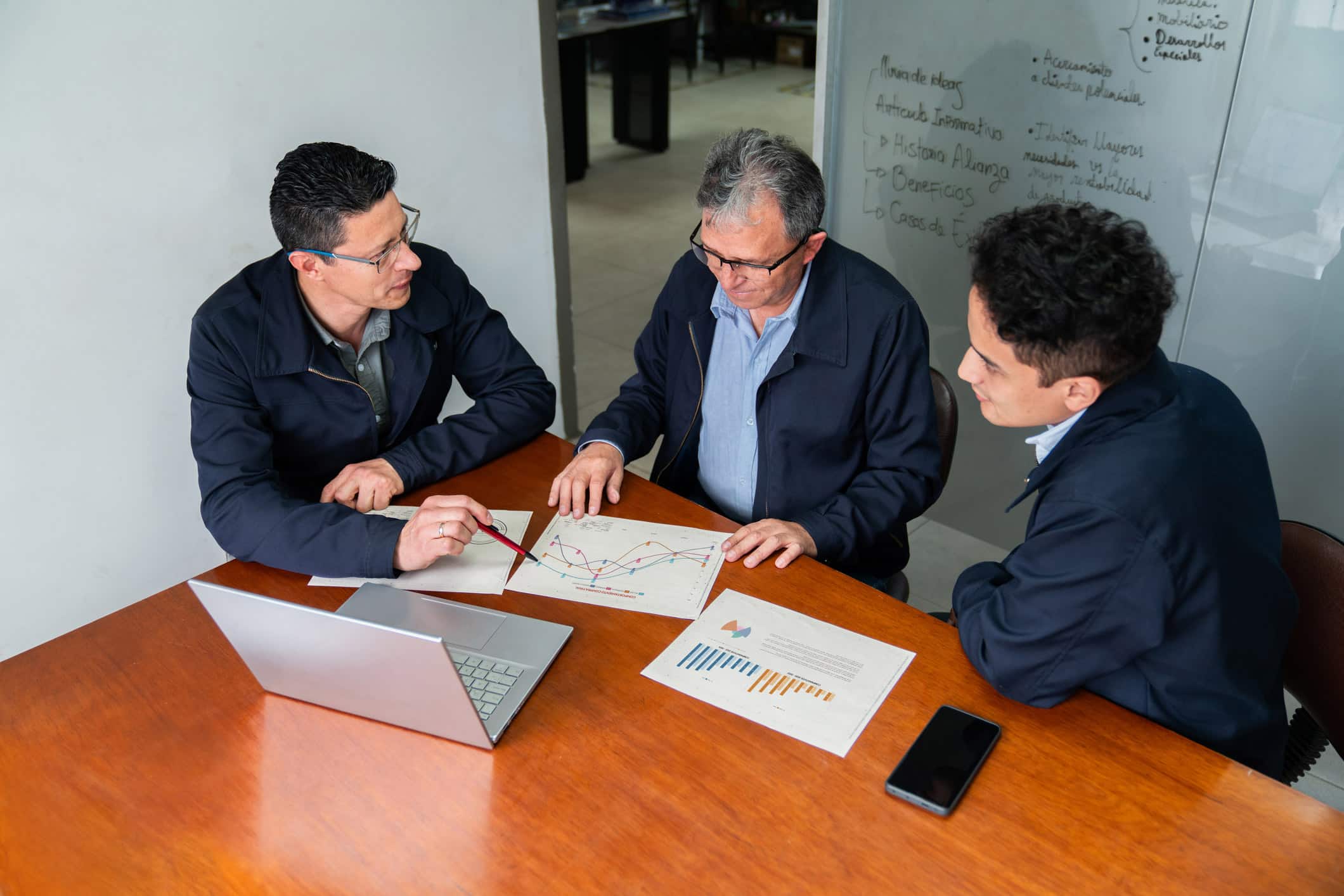Three men discuss charts and graphs at a table with Law Firm Marketing Consultants.