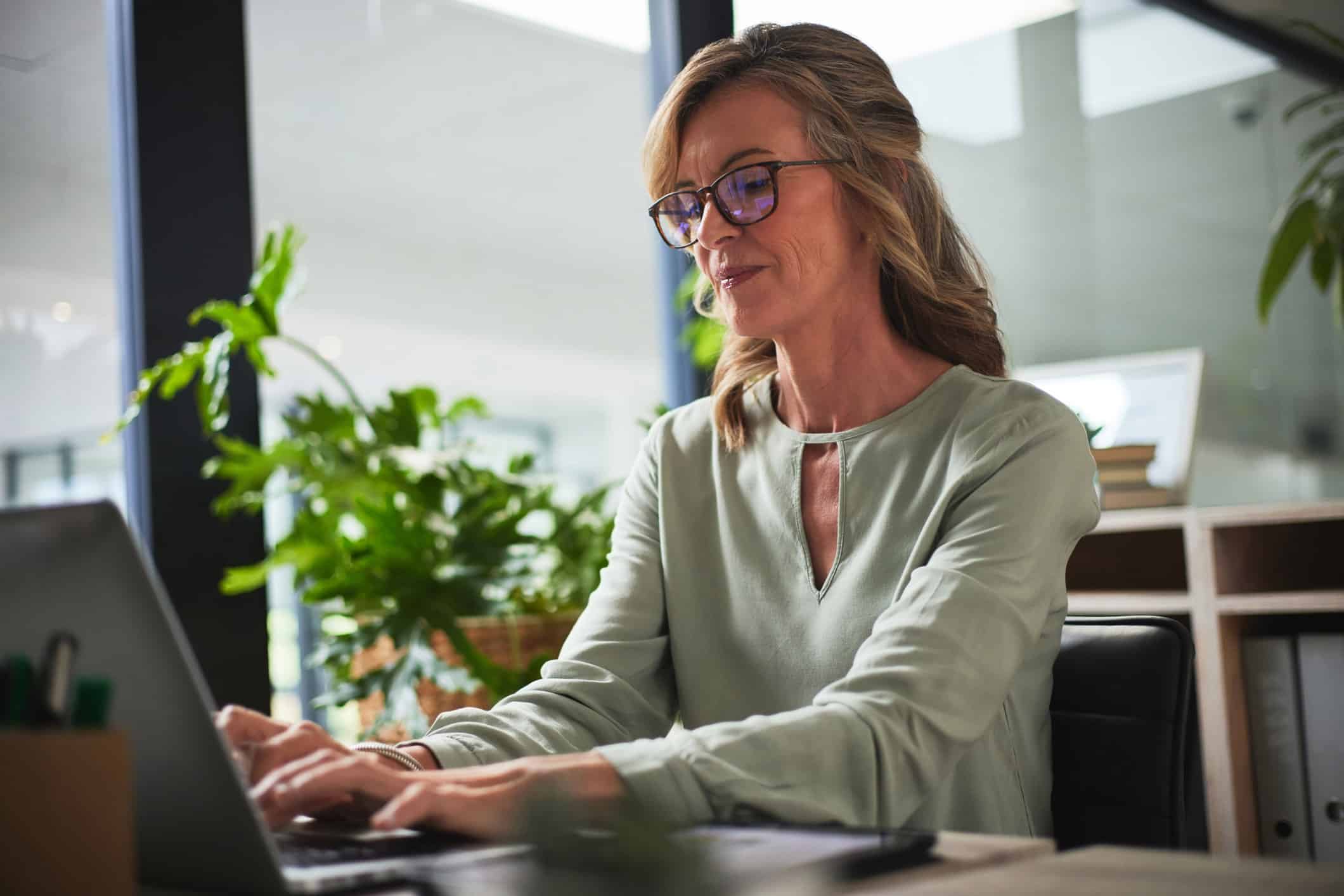 Woman with glasses working on forensic litigation at a laptop, surrounded by plants.