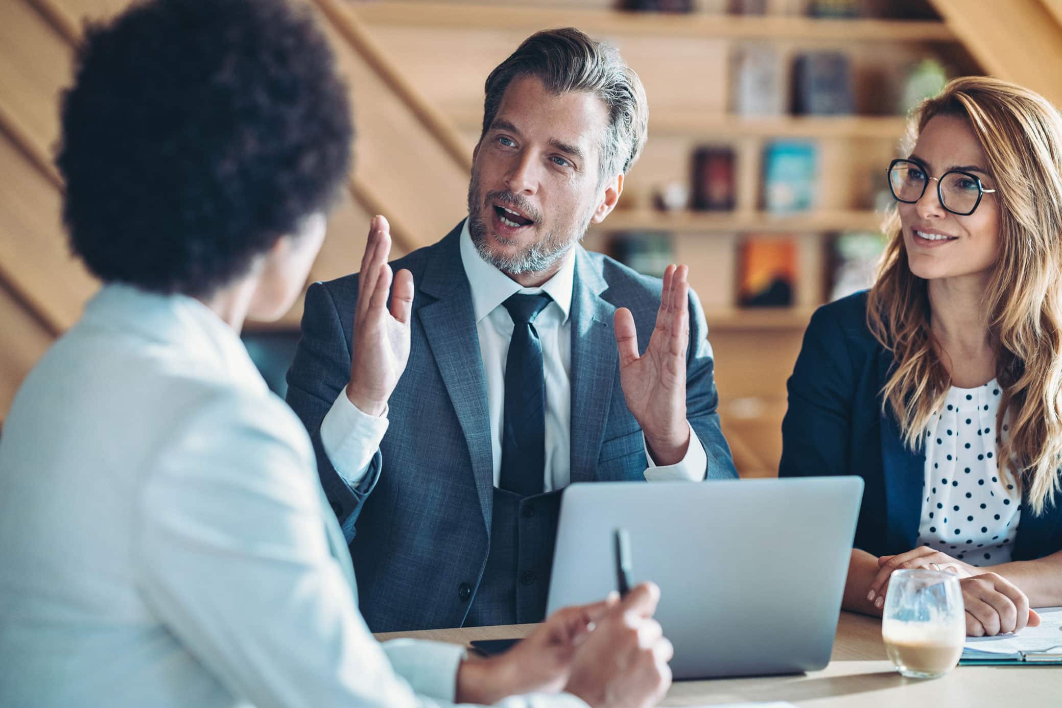 Three professionals discuss big data strategy; two listen as one speaks, laptop open on table.