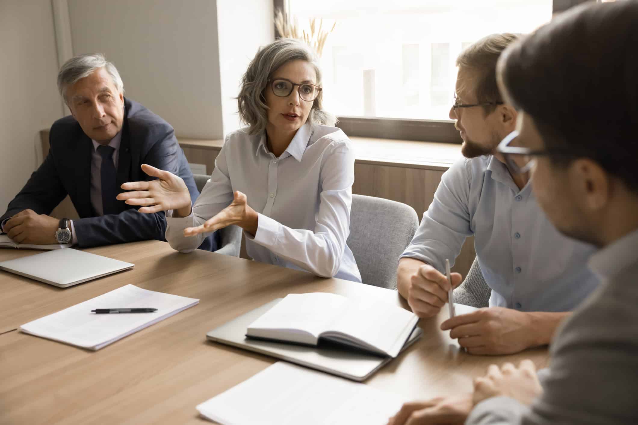 Four business professionals discuss M&A Integration Consulting at a conference table with documents.