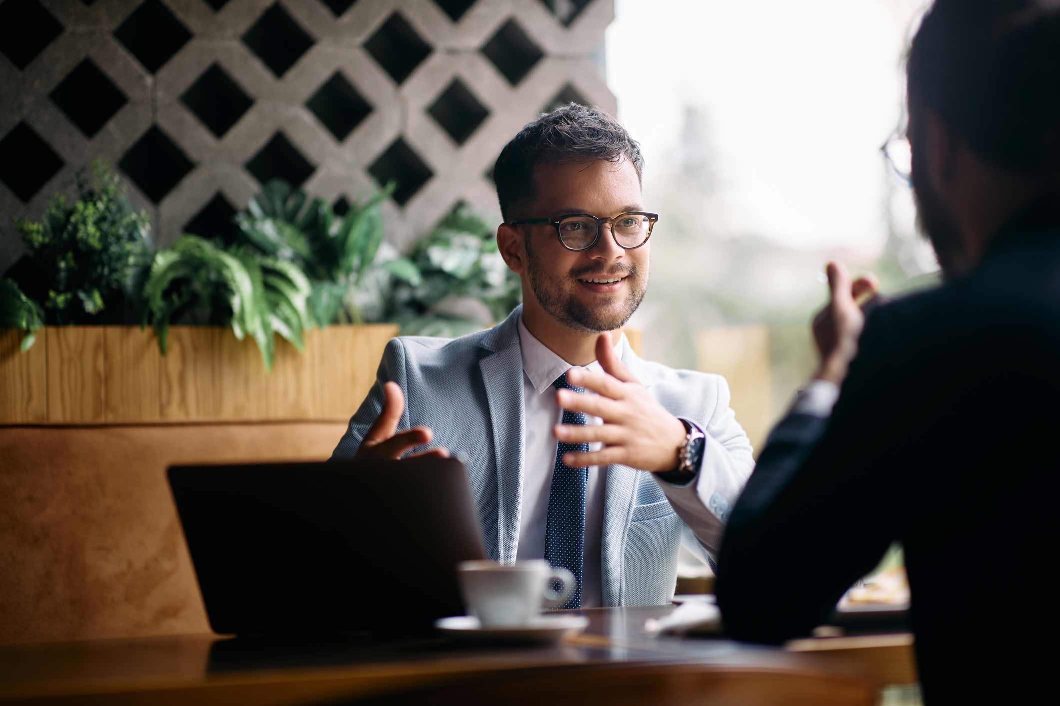 Two professionals discuss IAM Governance at a table with a laptop and coffee.