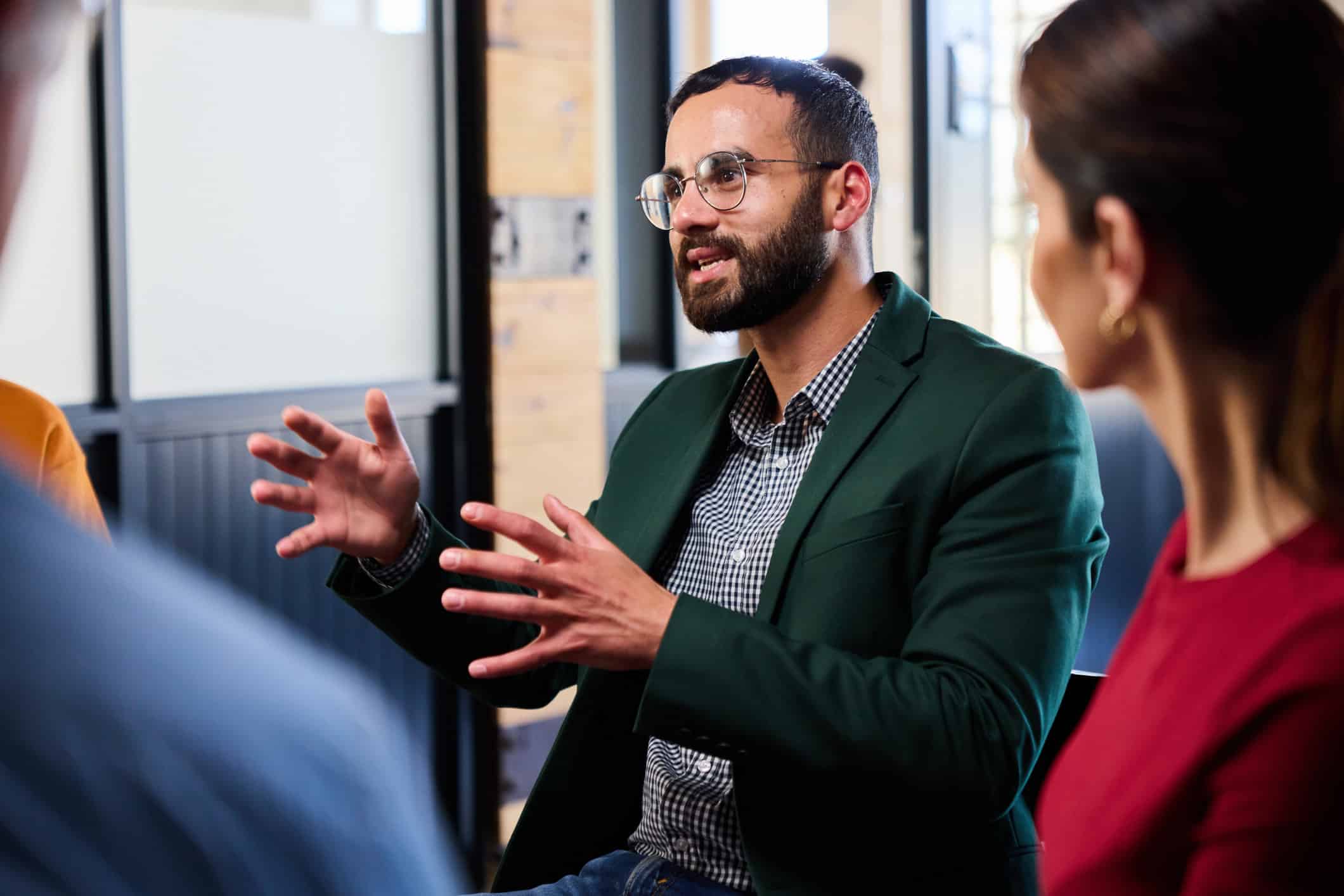 Man in a green blazer speaks during a group discussion at a trial strategy consulting firm.