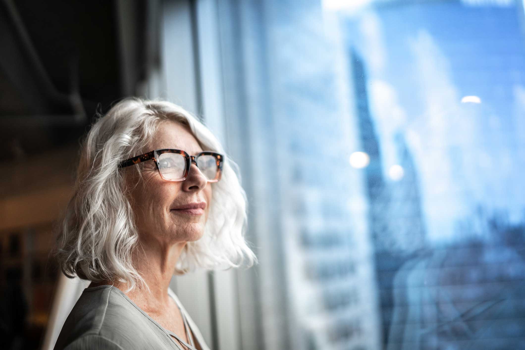 Older woman with white hair and glasses ponders Identity and Access Strategy by a city window.
