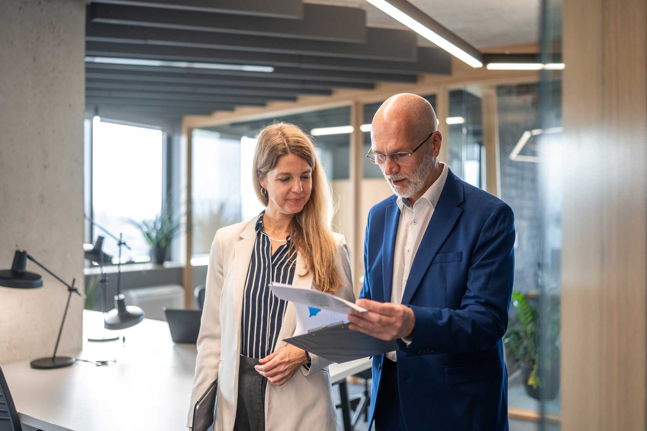 Two professionals review documents in a modern office, focusing on cybersecurity compliance.