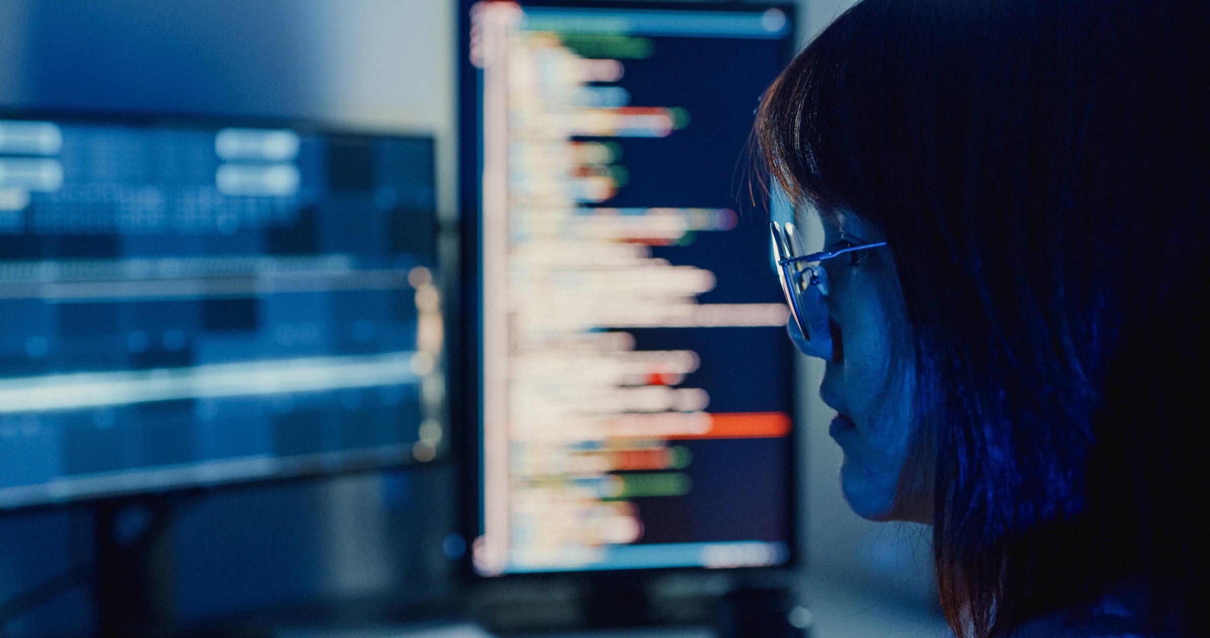Person with glasses analyzing eDiscovery Data Management on colorful screens in a dark room.