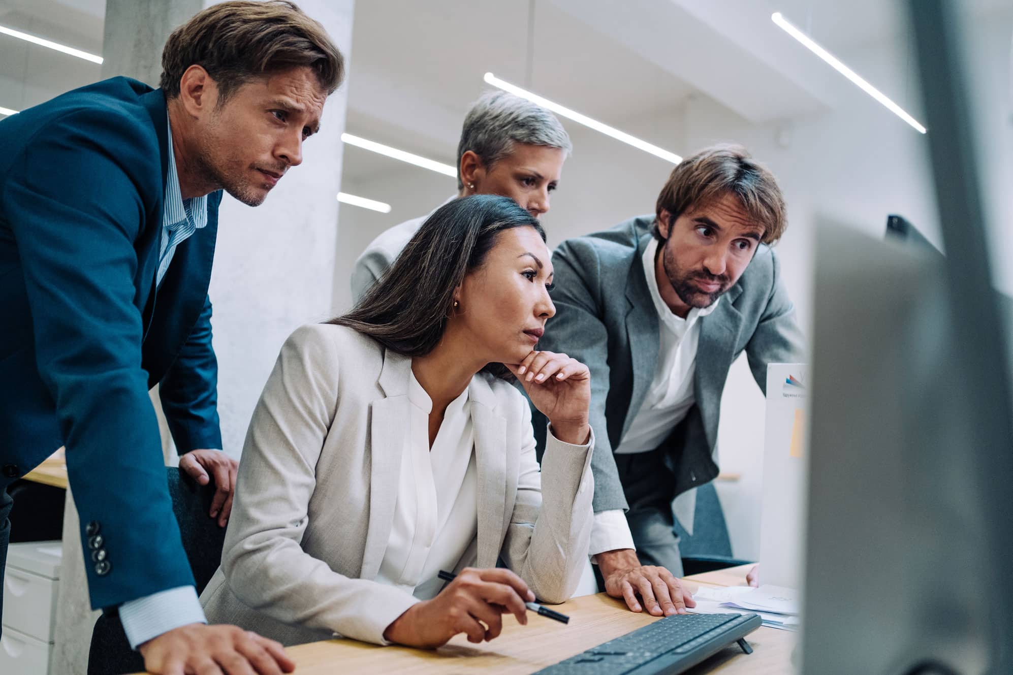 Four business professionals intently reviewing BI Consulting data on a computer screen in an office.