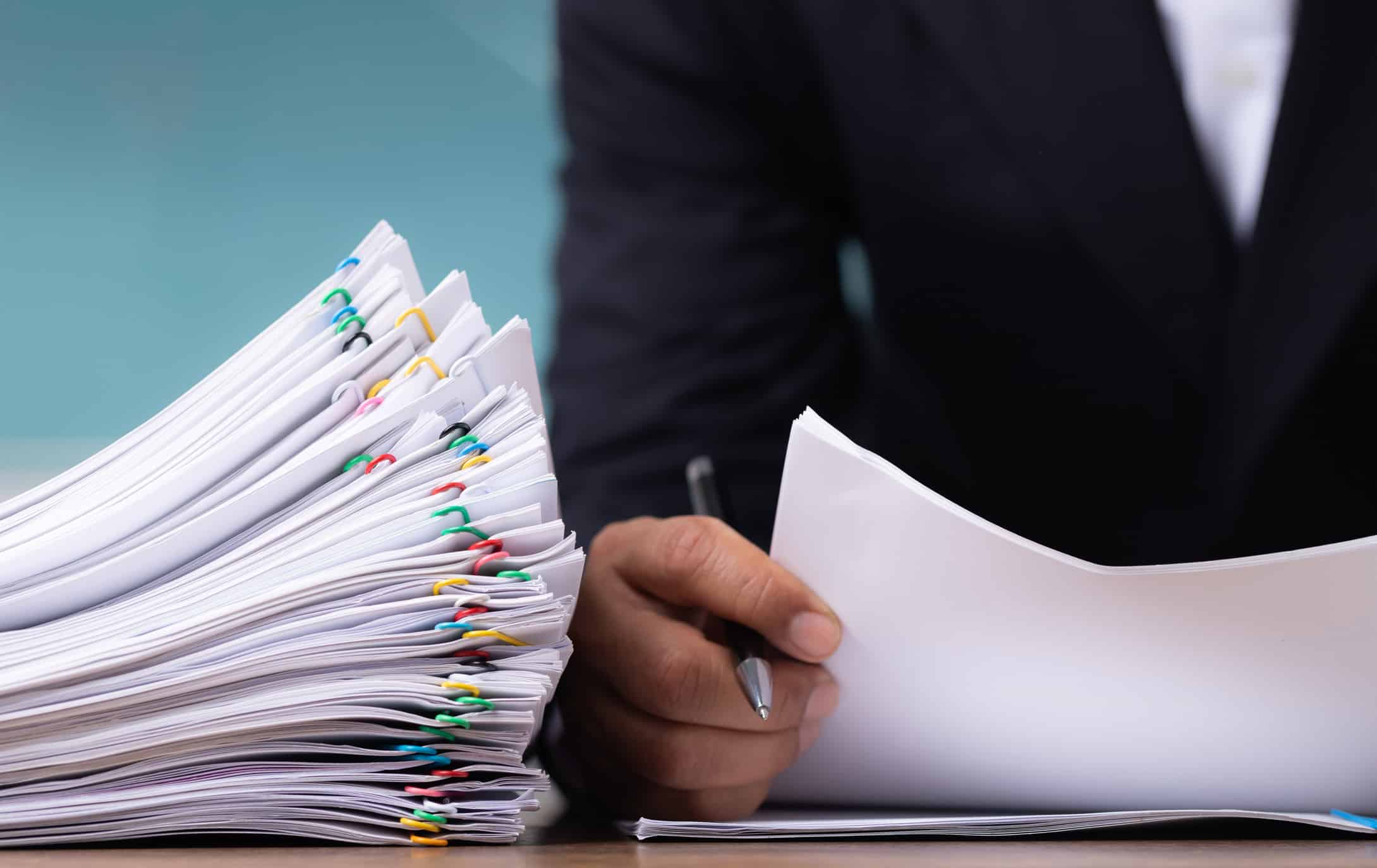 Person in suit reviews paperwork, exploring NLP for Law Firms beside a stack of documents.