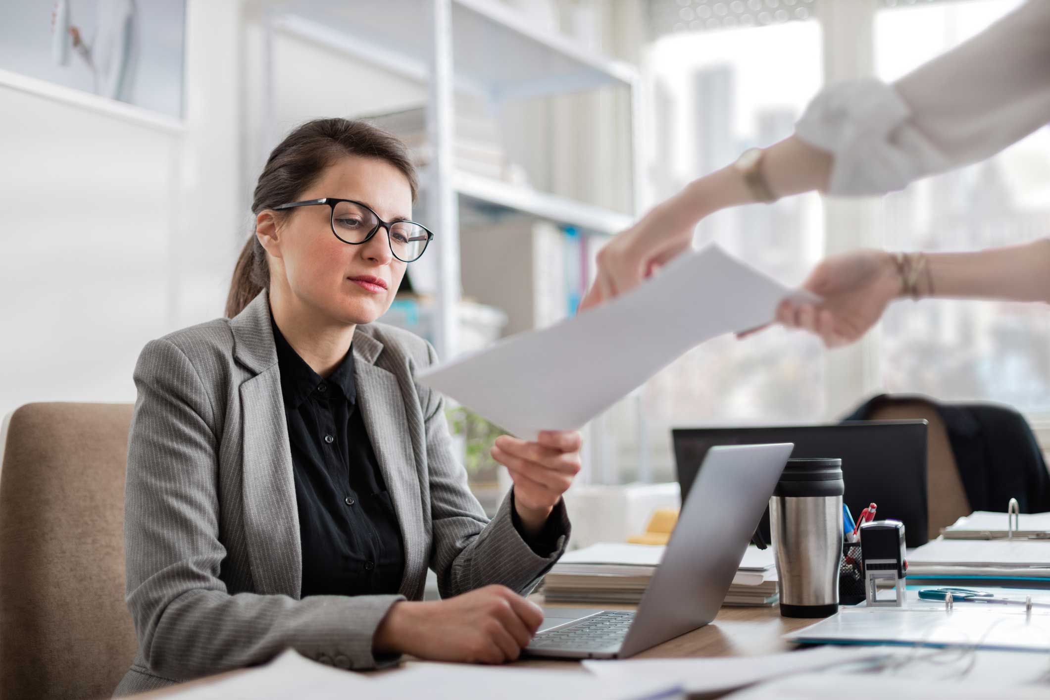 Woman in glasses reviews papers at desk, aided by AI Legal Document Analysis Consultants.