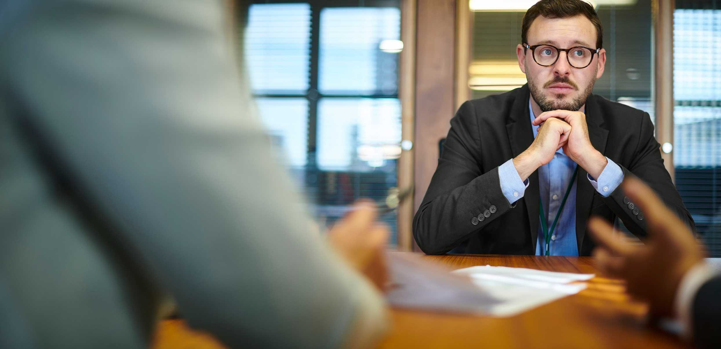 Man in glasses sits at a table, attentively listening to a cyber incident response services meeting.