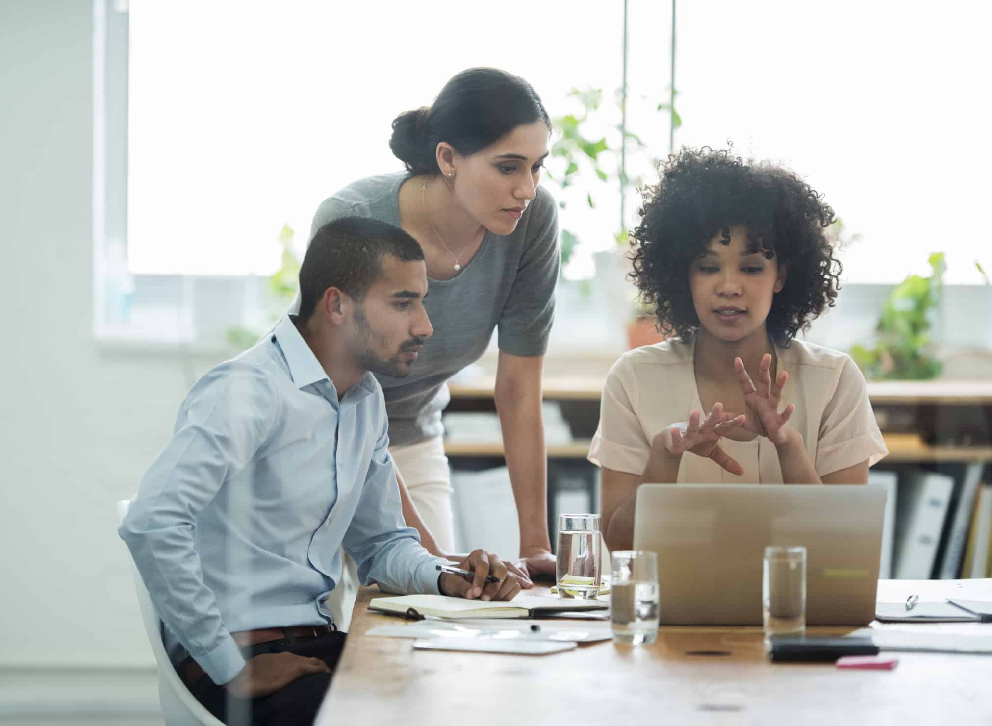 Three Economic Damages Consultants discuss something while looking at a laptop in a bright office.