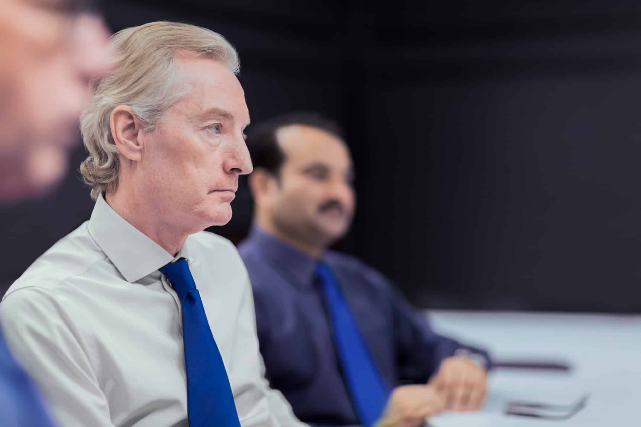 Serious businessmen in blue ties discuss Witness Preparation advisory at a conference table.