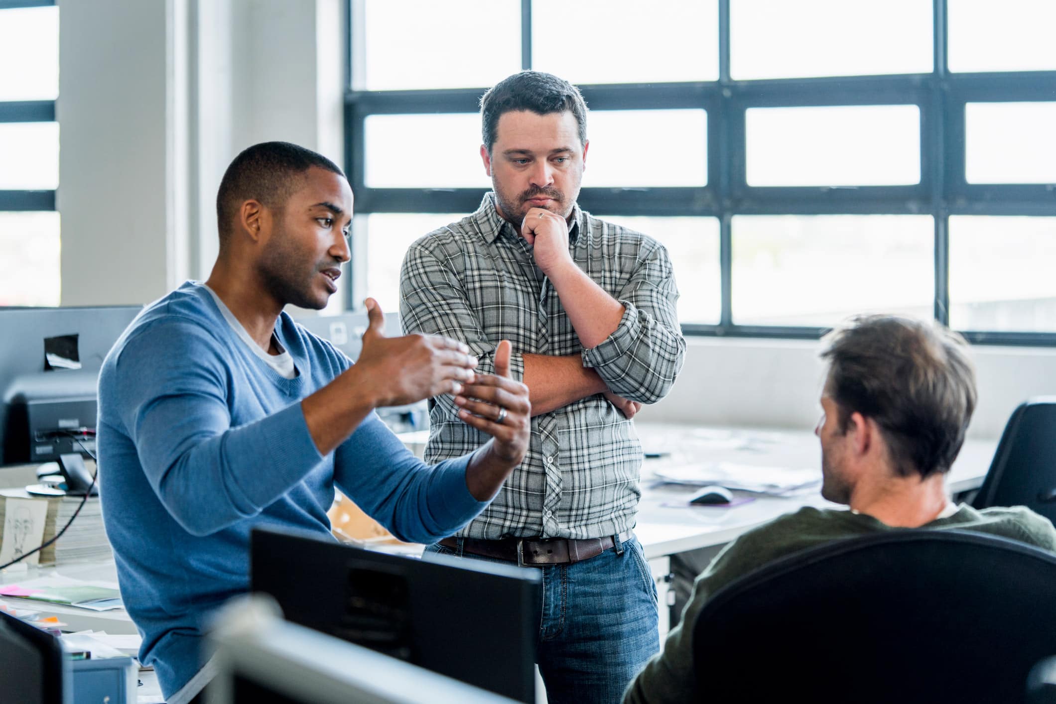 Three men in an Expense Reduction Consulting firm discuss strategies by a desk with computers.
