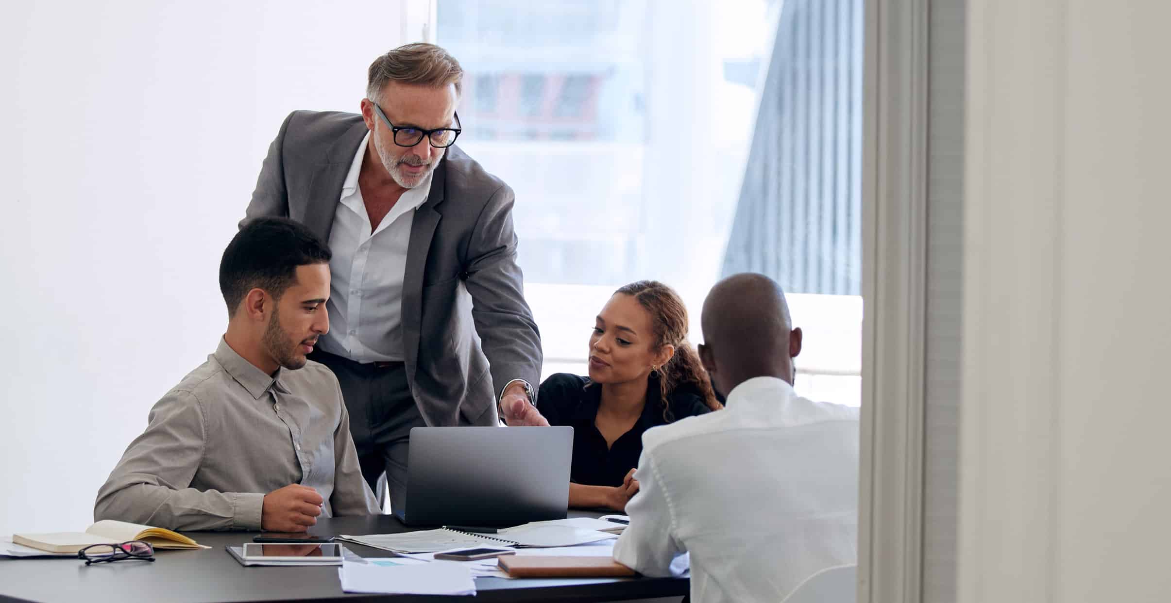Four Data Governance Consultants in a meeting room, discussing something on a laptop.